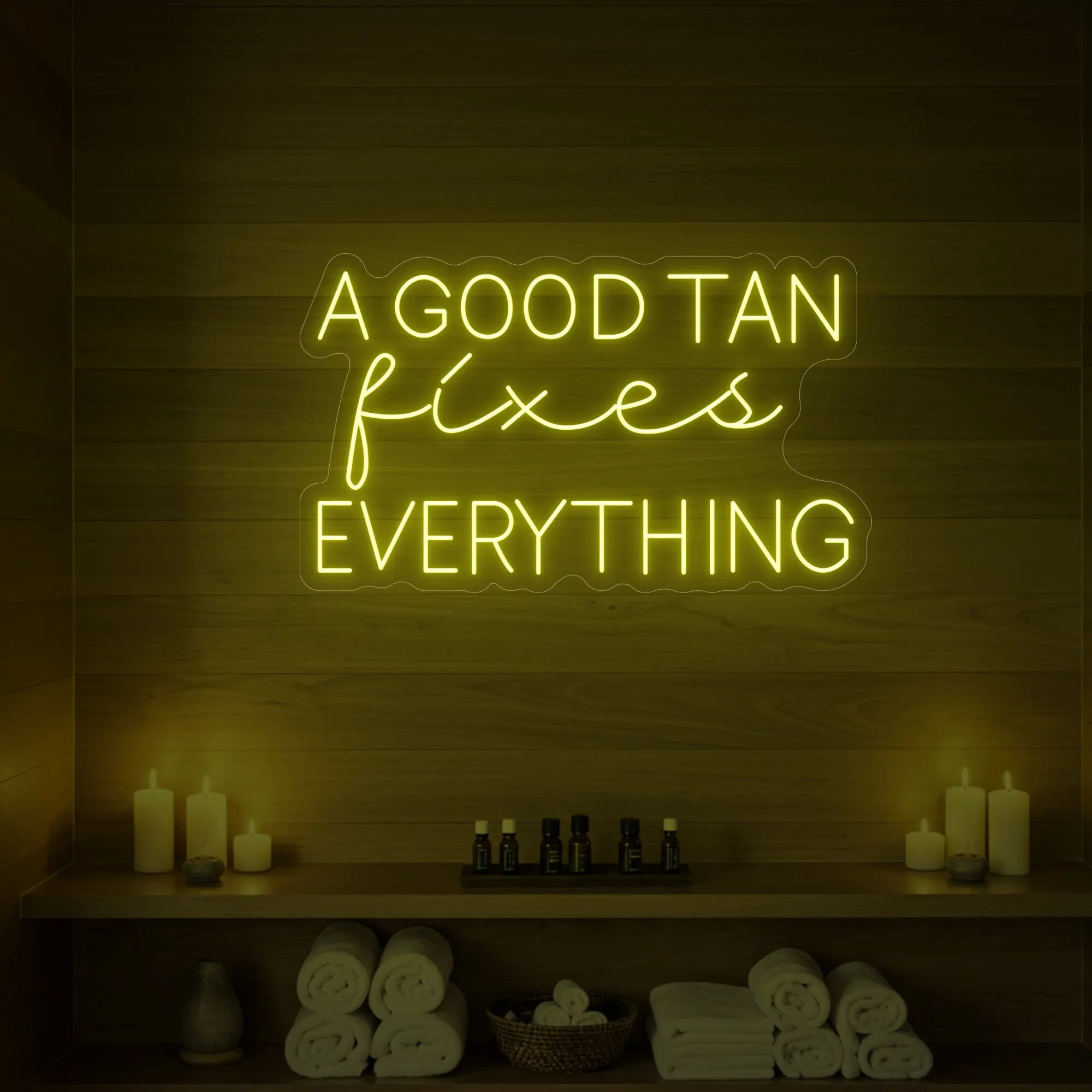 Photo of the 'A GOOD TAN fixes EVERYTHING' neon sign glowing in lemon yellow against a styled interior wall.
