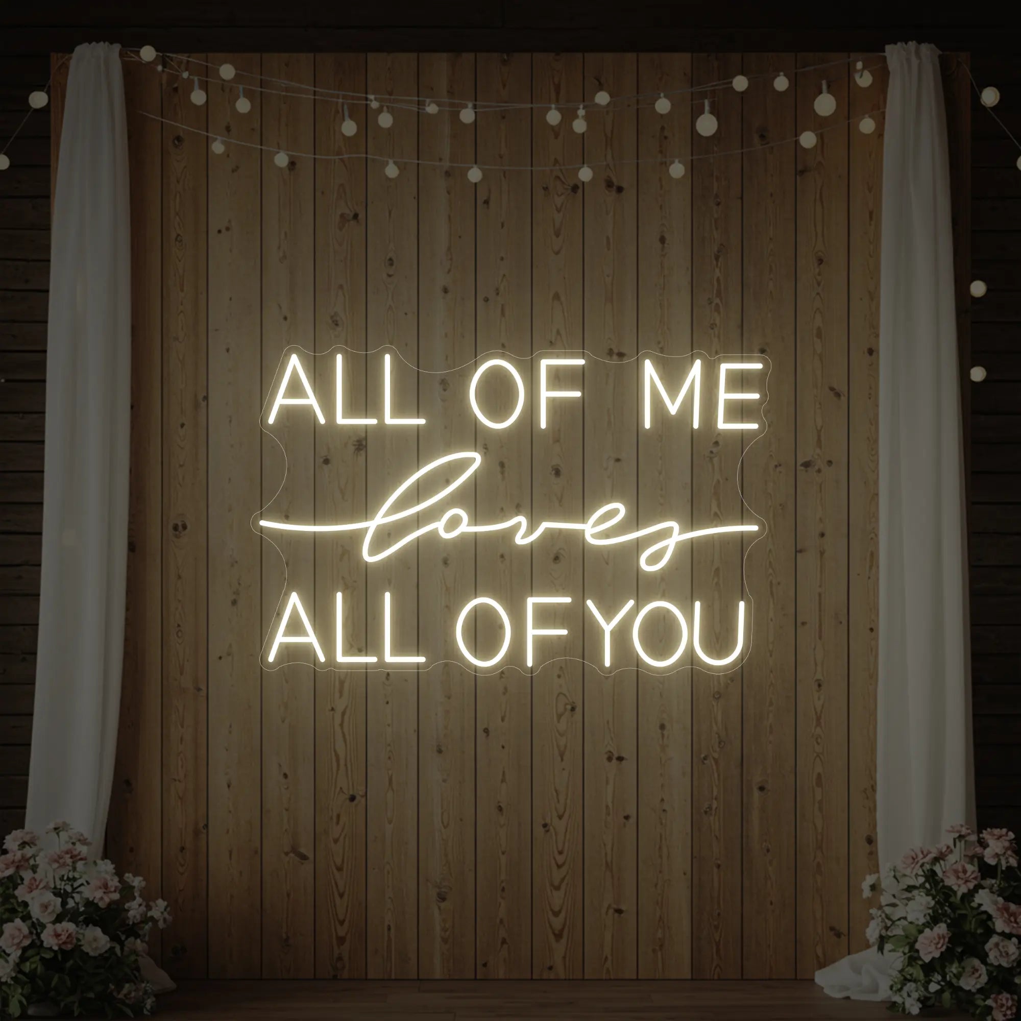 Photo of the 'All Of Me Love All Of You' neon sign glowing in warm white against a styled interior wall.