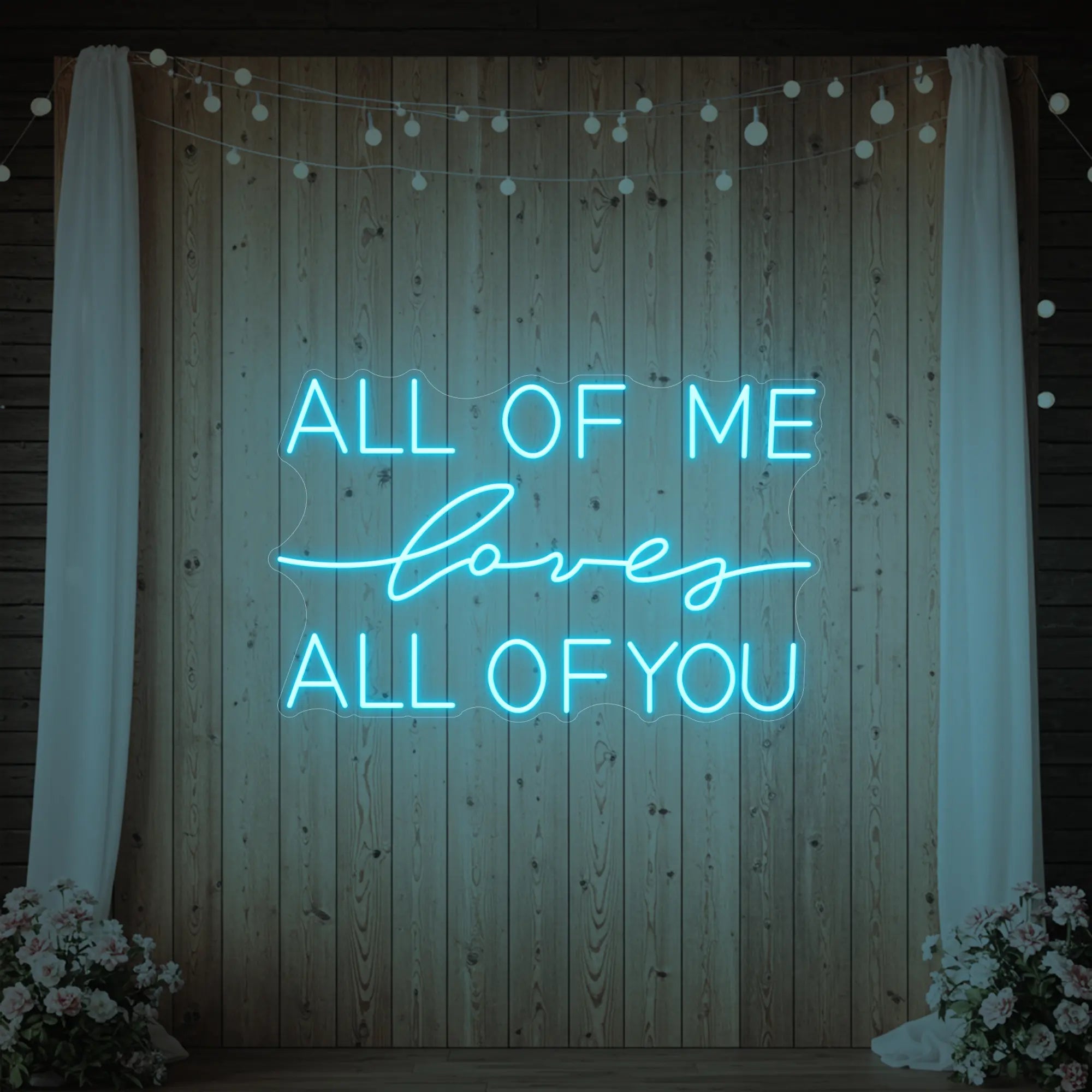 Photo of the 'All Of Me Love All Of You' neon sign glowing in ice blue against a styled interior wall.