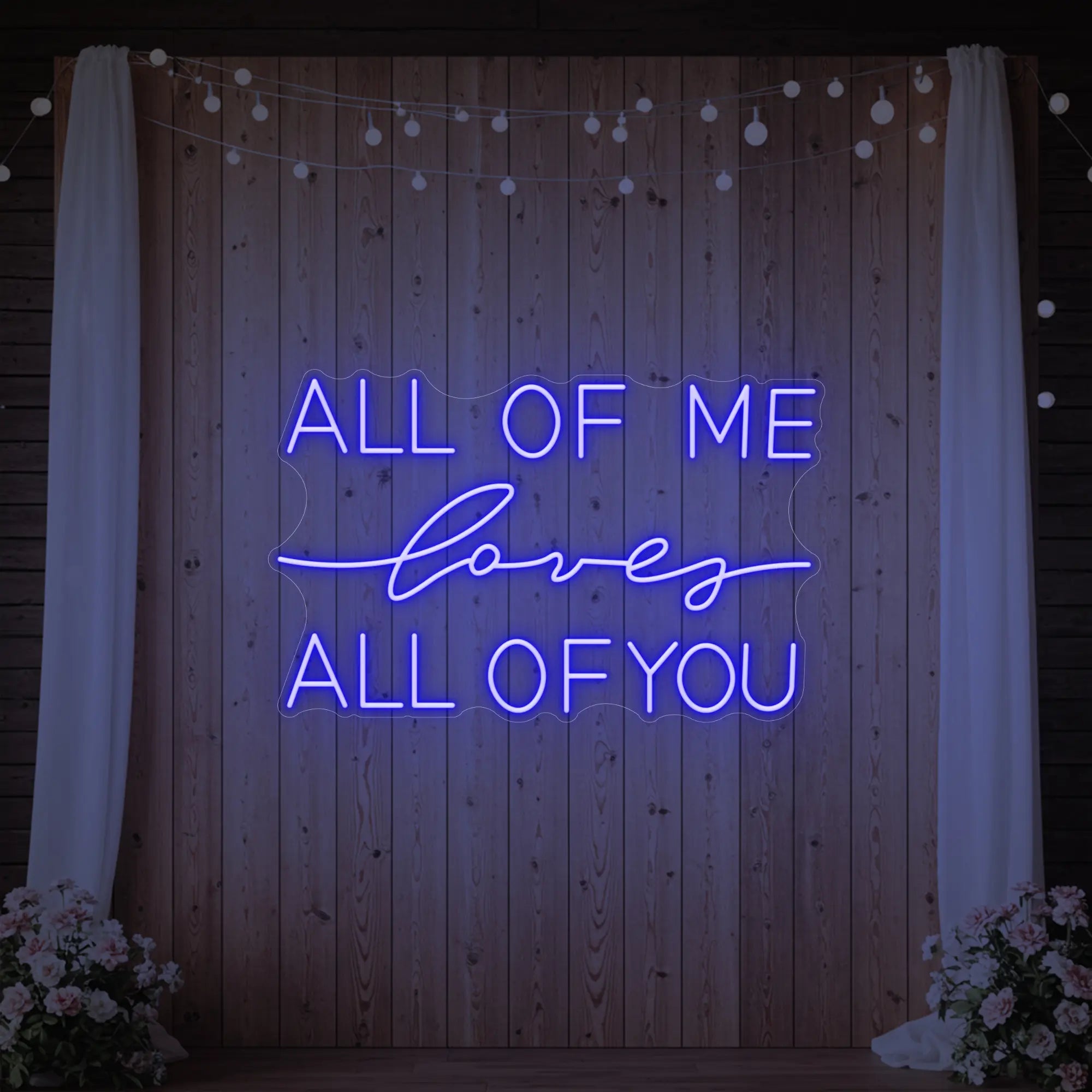 Photo of the 'All Of Me Love All Of You' neon sign glowing in deep blue against a styled interior wall.
