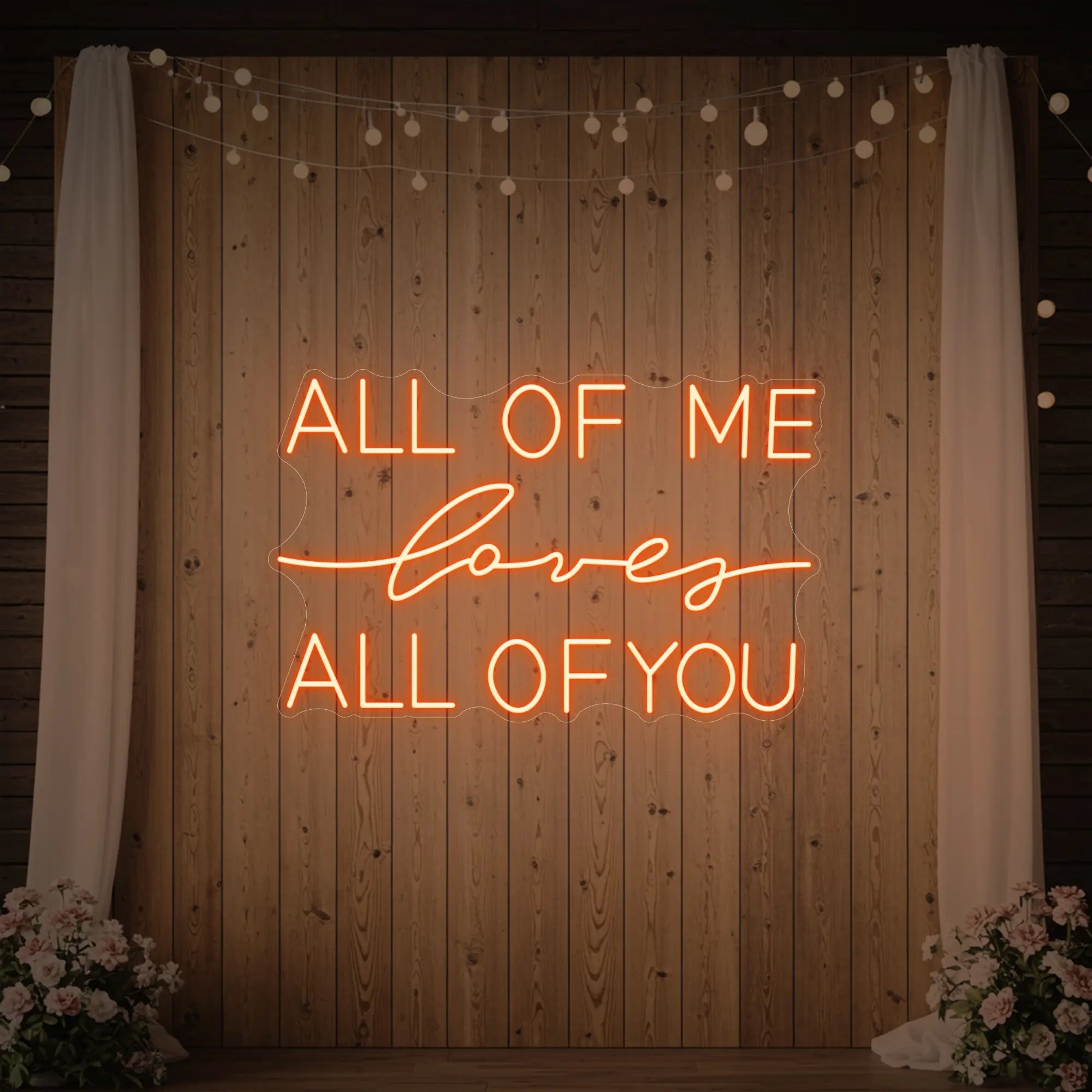 Photo of the 'All Of Me Love All Of You' neon sign glowing in golden yellow against a styled interior wall.
