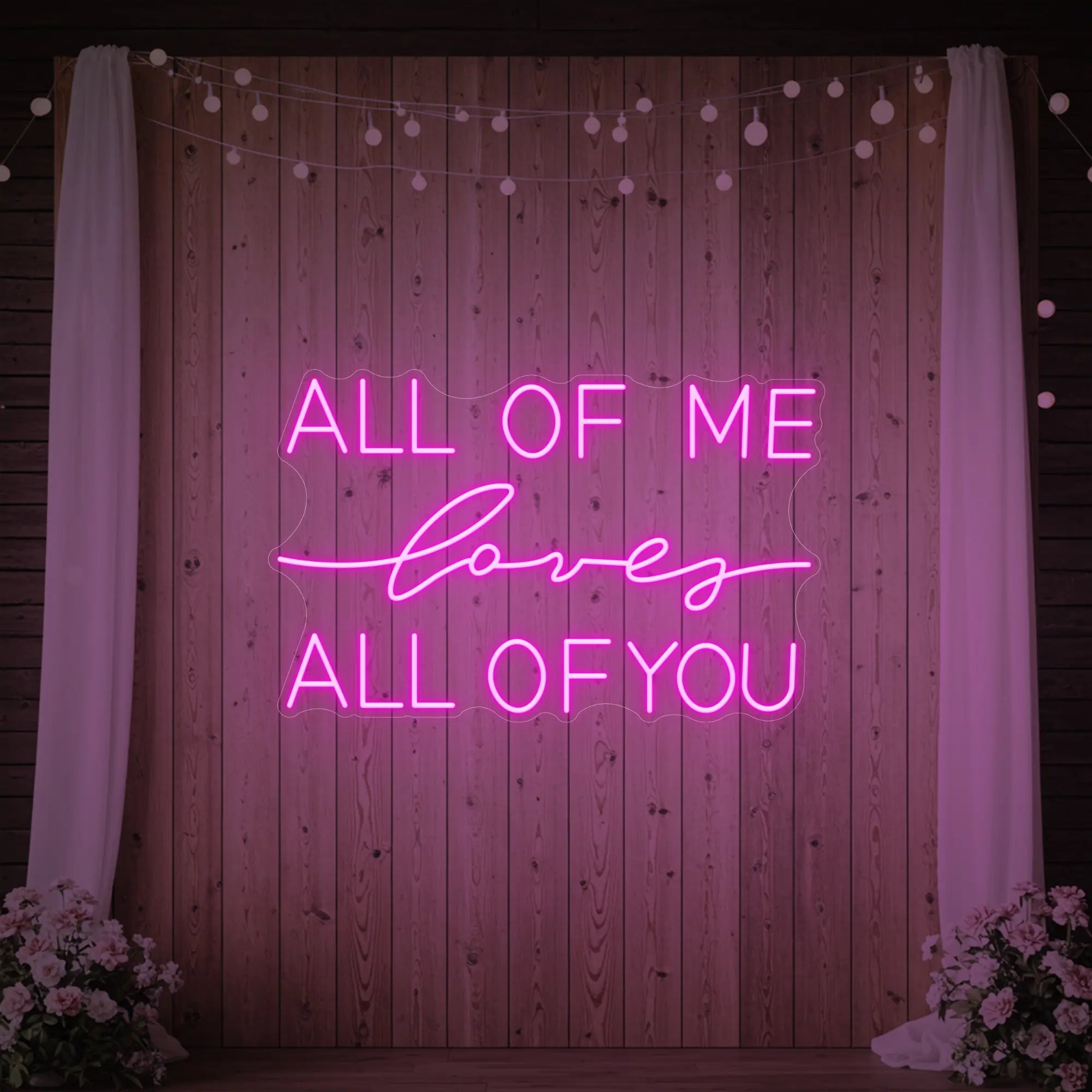 Photo of the 'All Of Me Love All Of You' neon sign glowing in light pink against a styled interior wall.