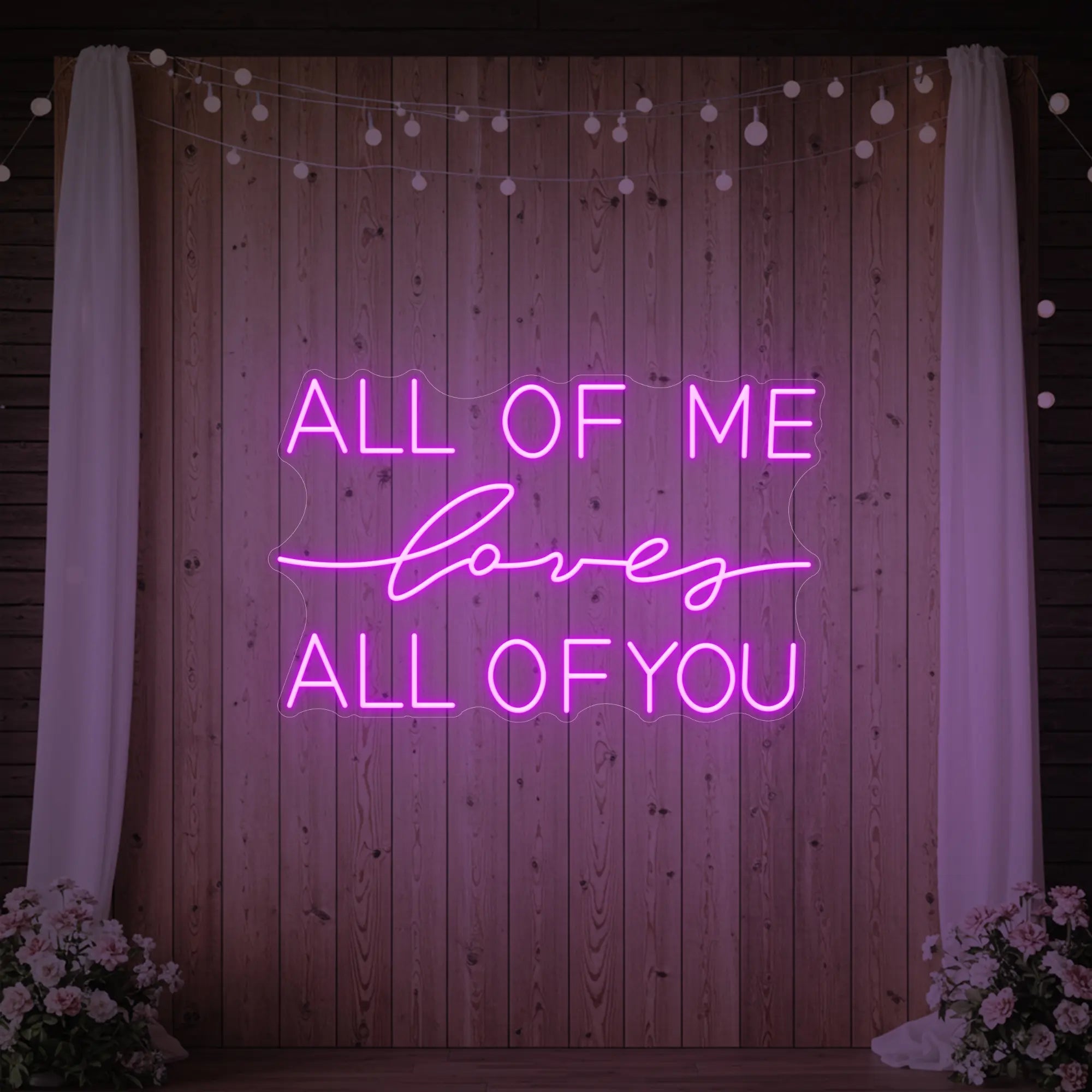 Photo of the 'All Of Me Love All Of You' neon sign glowing in deep pink against a styled interior wall.