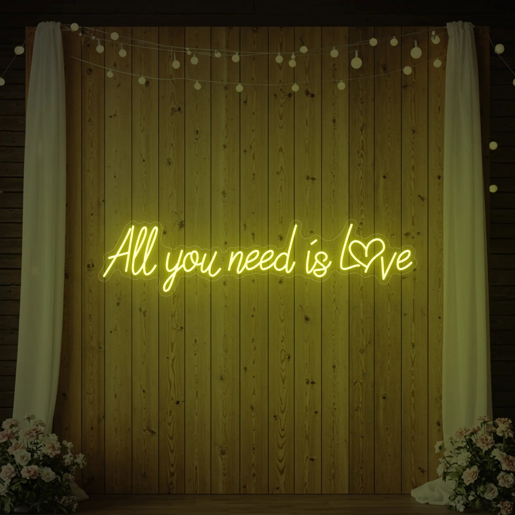 Photo of the 'All You Need Is Love Heart' neon sign glowing in lemon yellow against a styled interior wall.