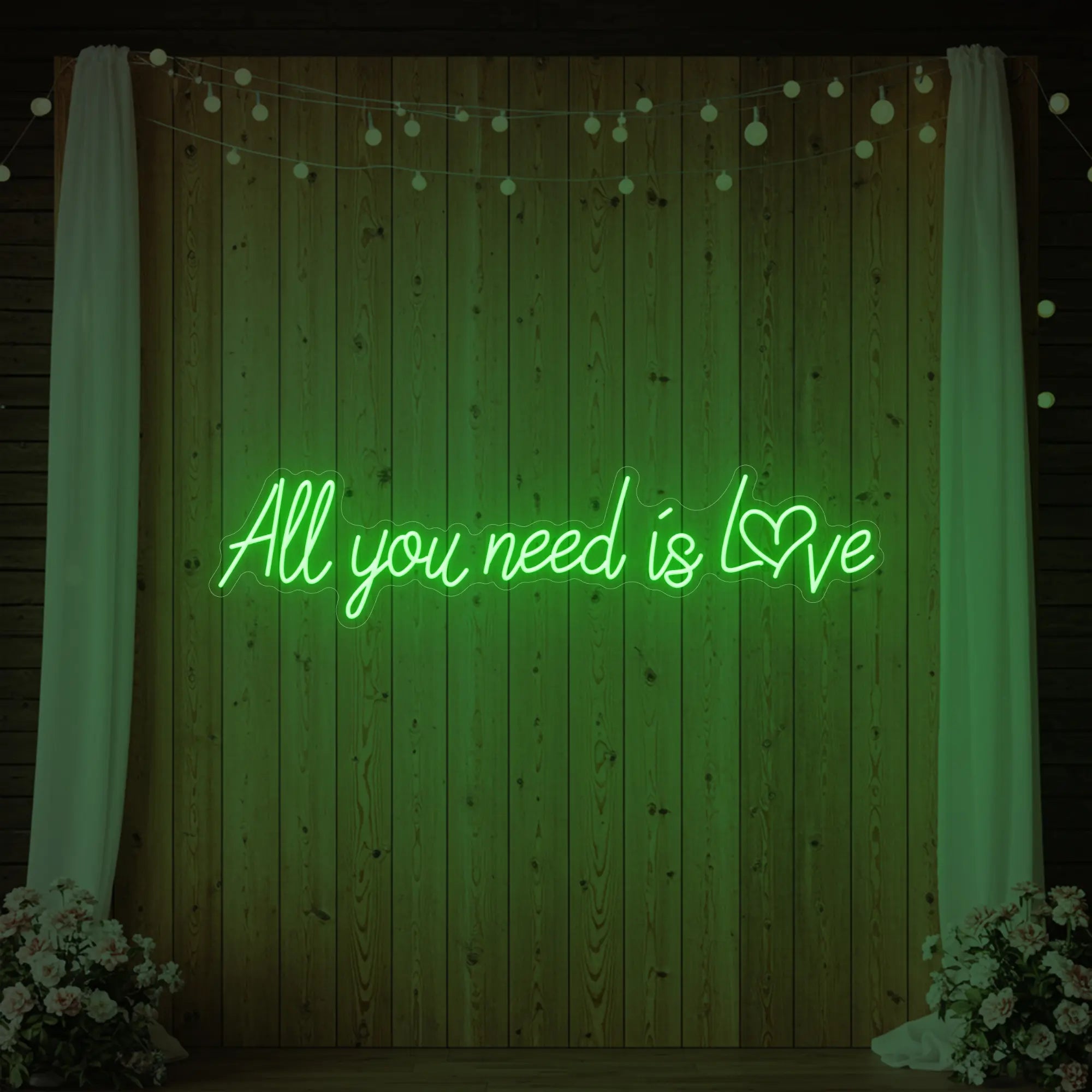 Photo of the 'All You Need Is Love Heart' neon sign glowing in green against a styled interior wall.