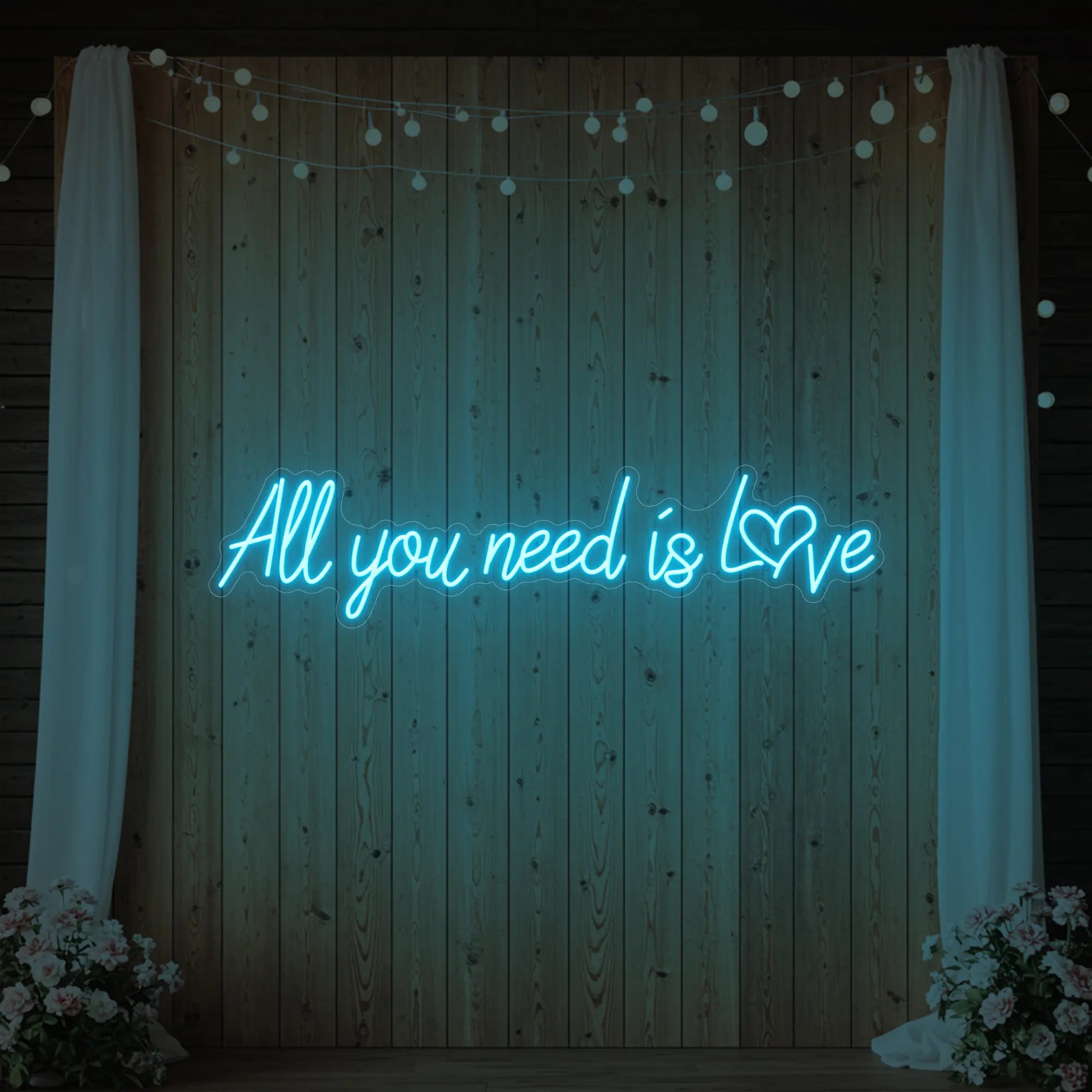 Photo of the 'All You Need Is Love Heart' neon sign glowing in ice blue against a styled interior wall.