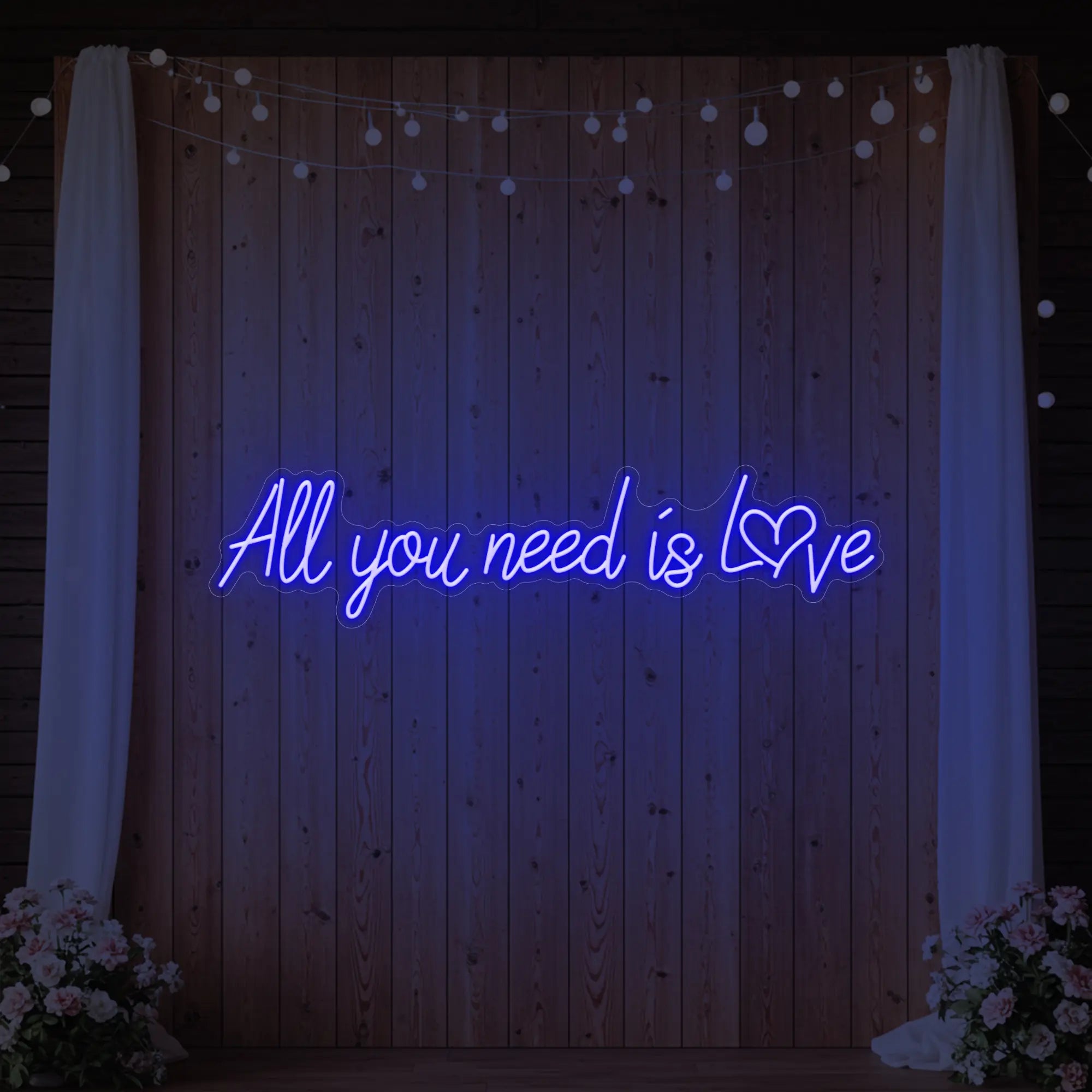 Photo of the 'All You Need Is Love Heart' neon sign glowing in deep blue against a styled interior wall.