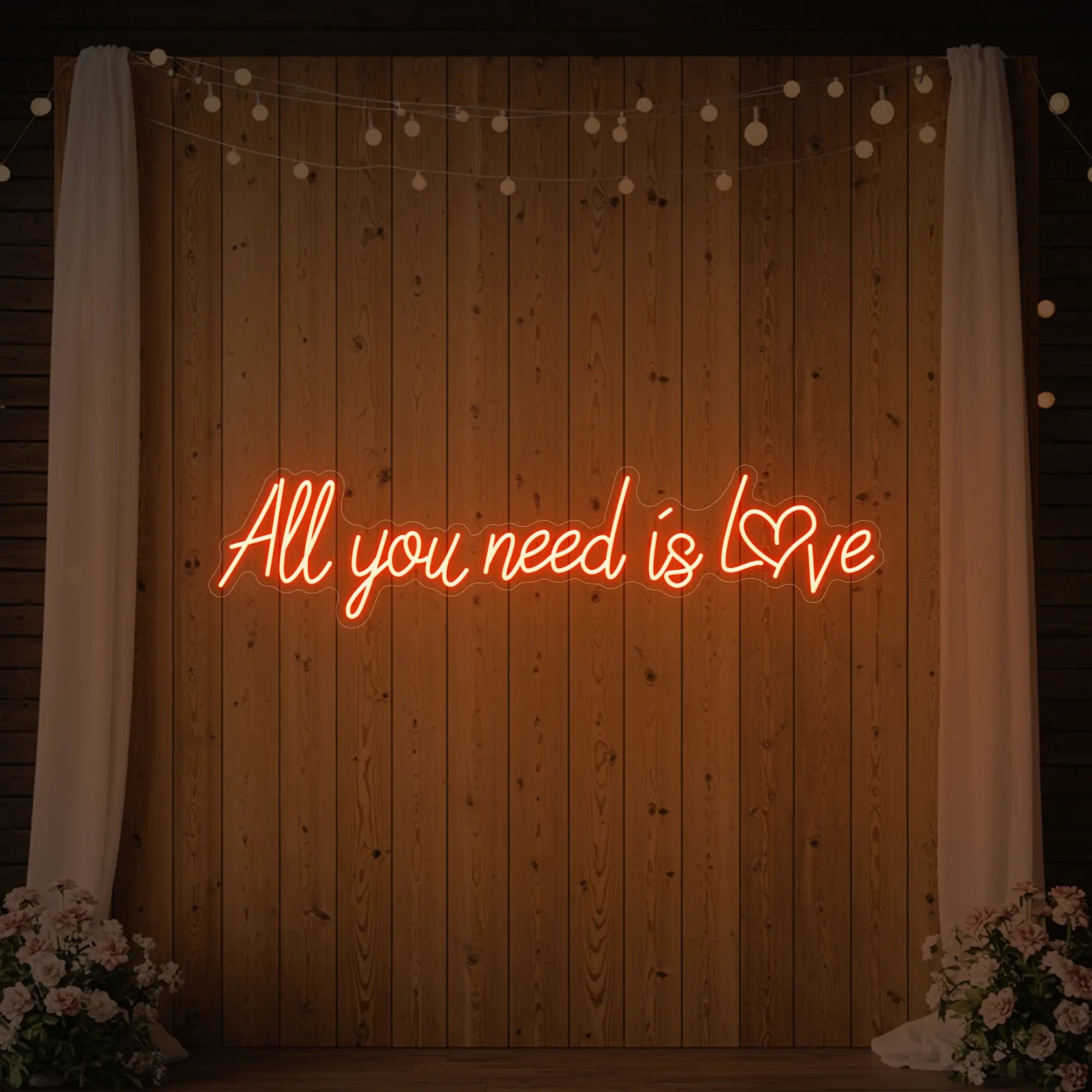 Photo of the 'All You Need Is Love Heart' neon sign glowing in golden yellow against a styled interior wall.
