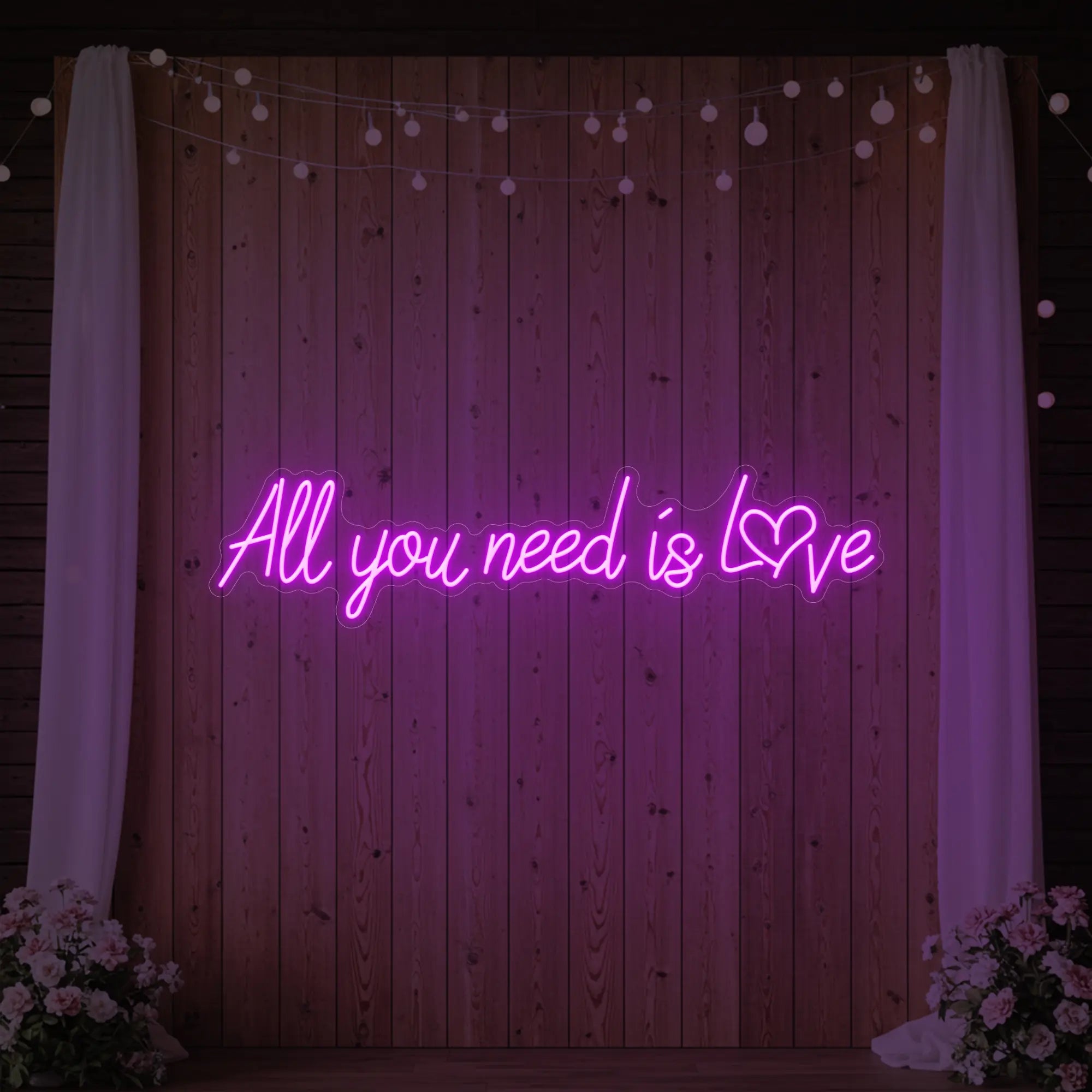Photo of the 'All You Need Is Love Heart' neon sign glowing in deep pink against a styled interior wall.