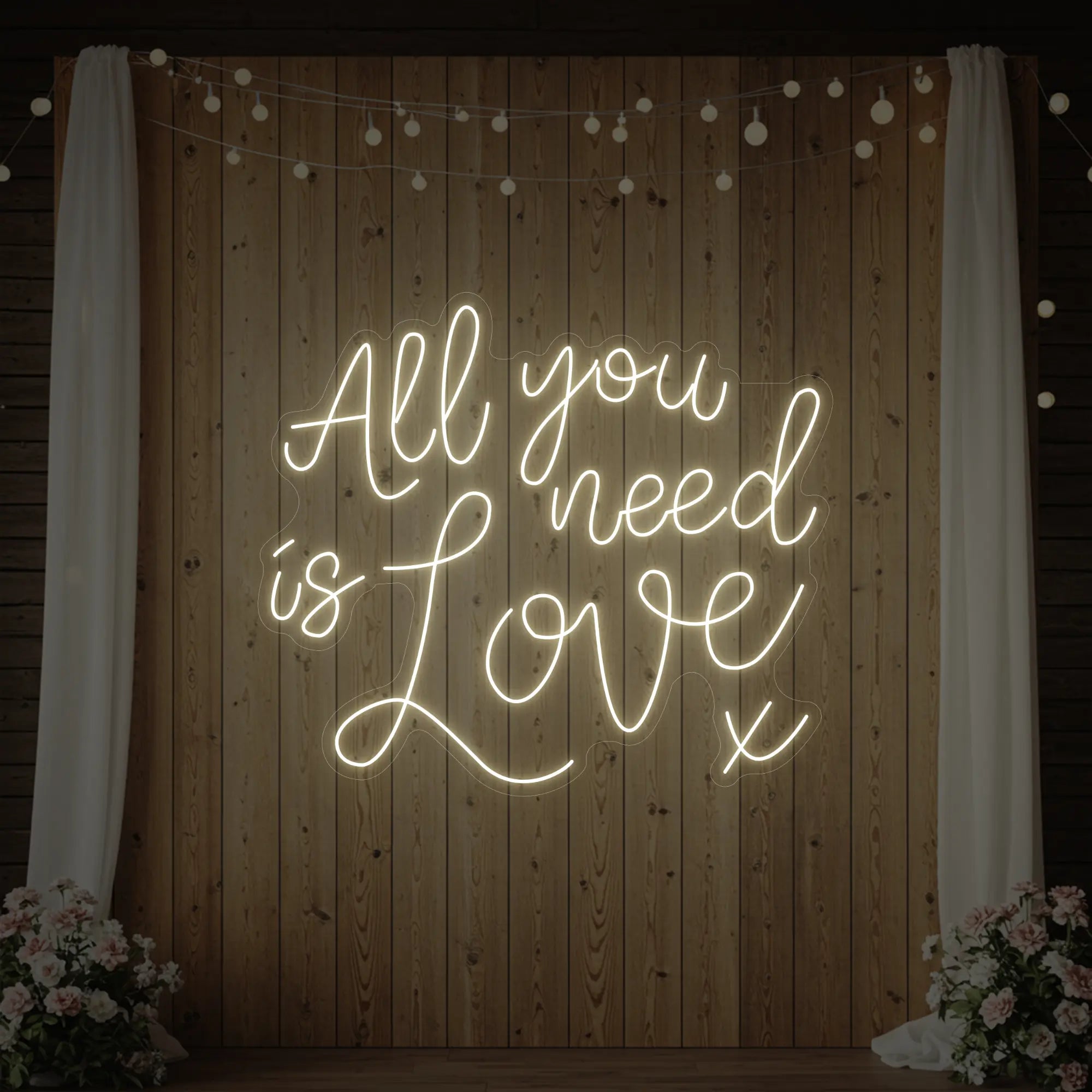 Photo of the 'All You Need Is Love V1' neon sign glowing in warm white against a styled interior wall.