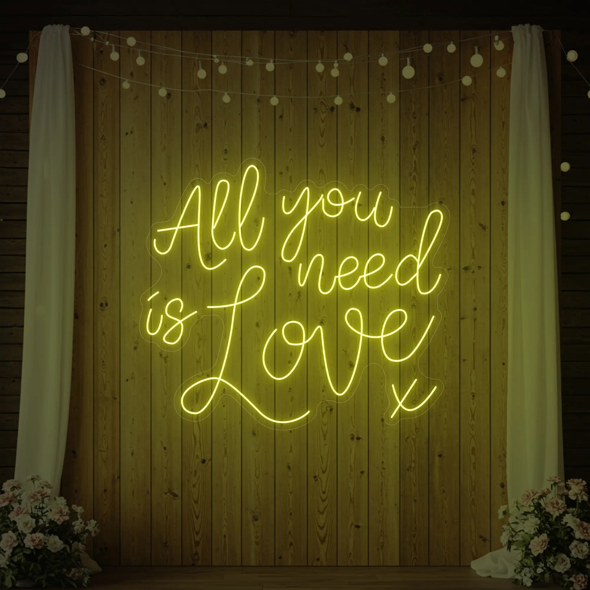 Photo of the 'All You Need Is Love V1' neon sign glowing in lemon yellow against a styled interior wall.