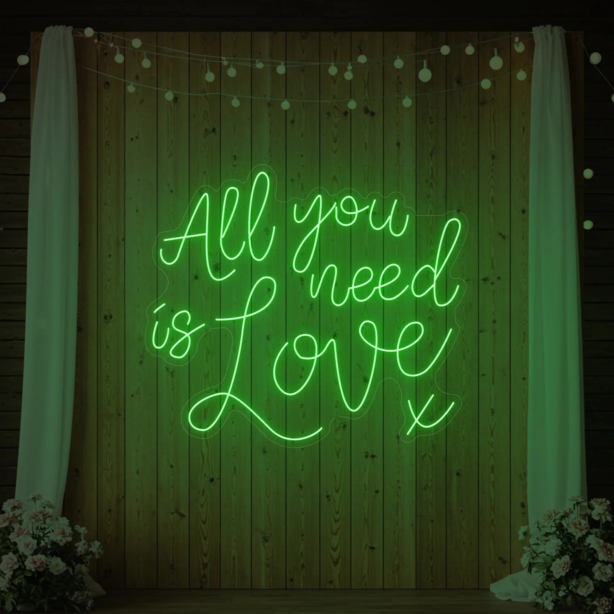 Photo of the 'All You Need Is Love V1' neon sign glowing in green against a styled interior wall.