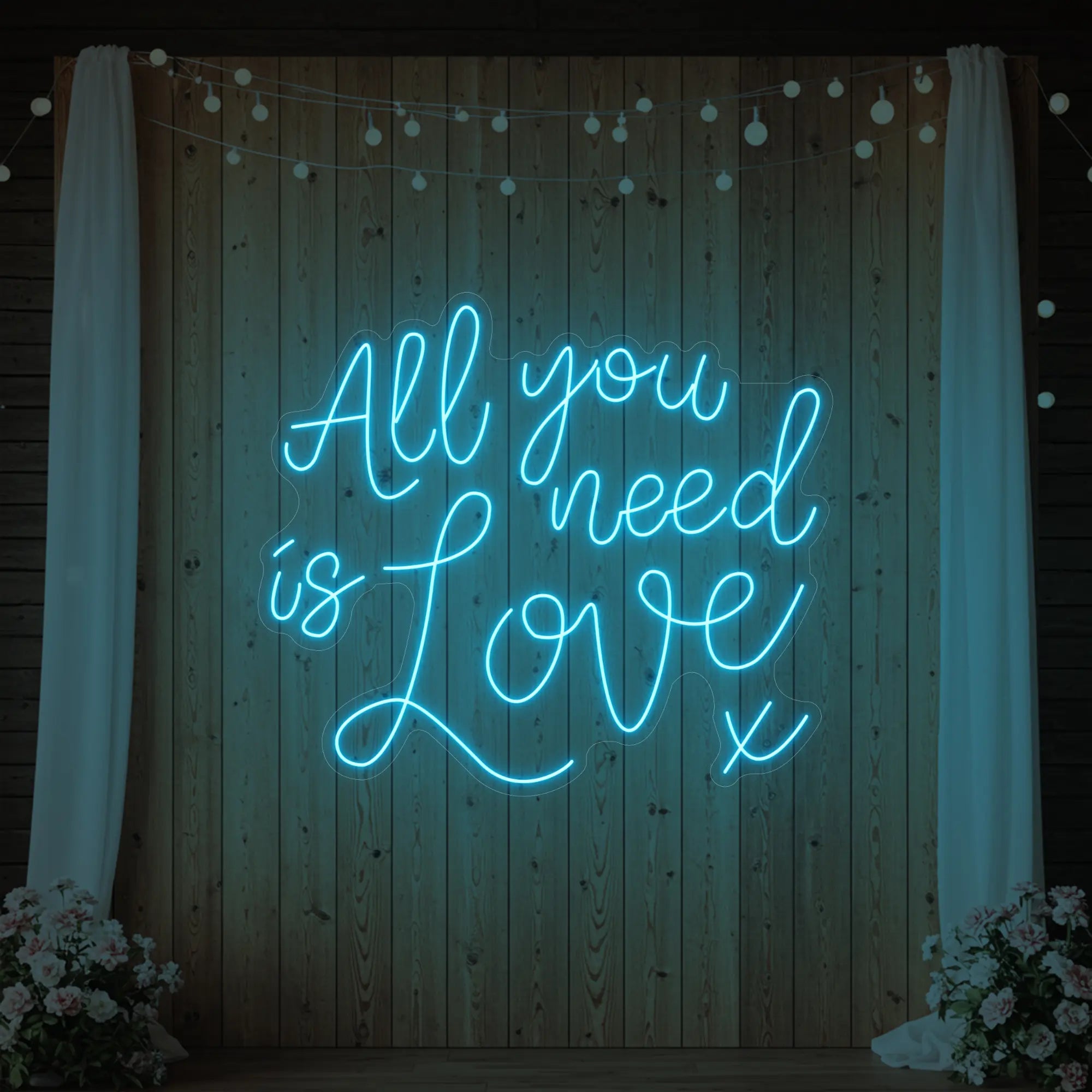 Photo of the 'All You Need Is Love V1' neon sign glowing in ice blue against a styled interior wall.