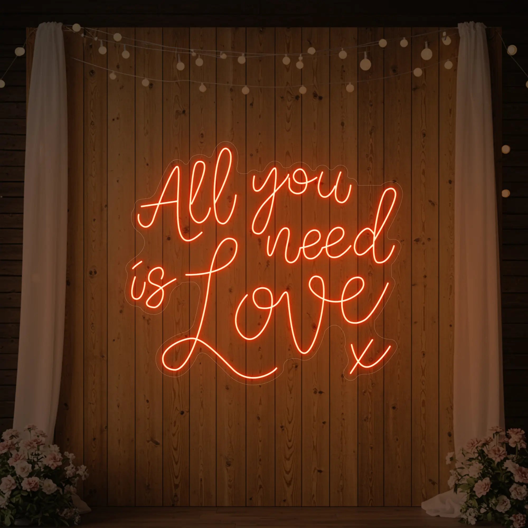 Photo of the 'All You Need Is Love V1' neon sign glowing in golden yellow against a styled interior wall.