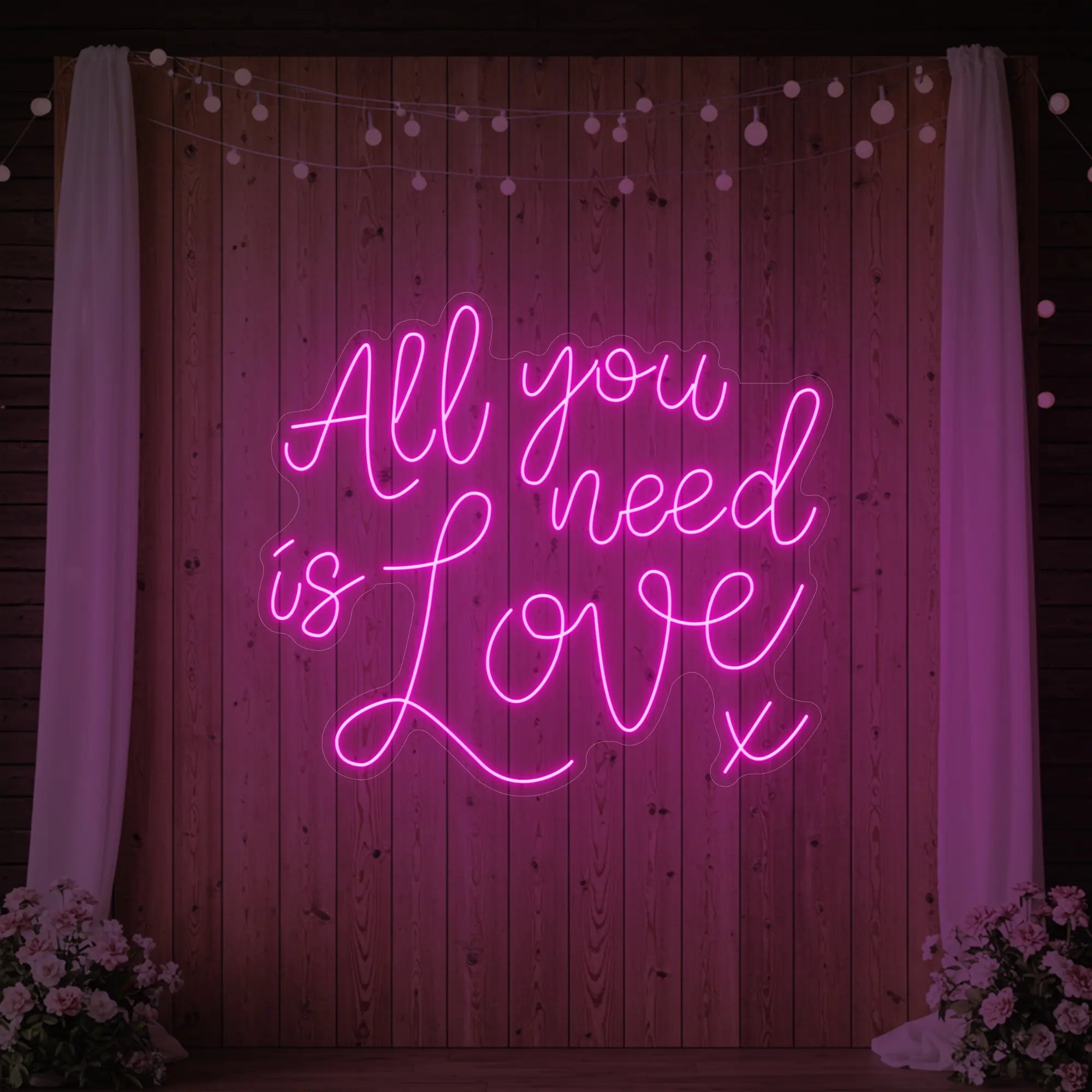 Photo of the 'All You Need Is Love V1' neon sign glowing in light pink against a styled interior wall.
