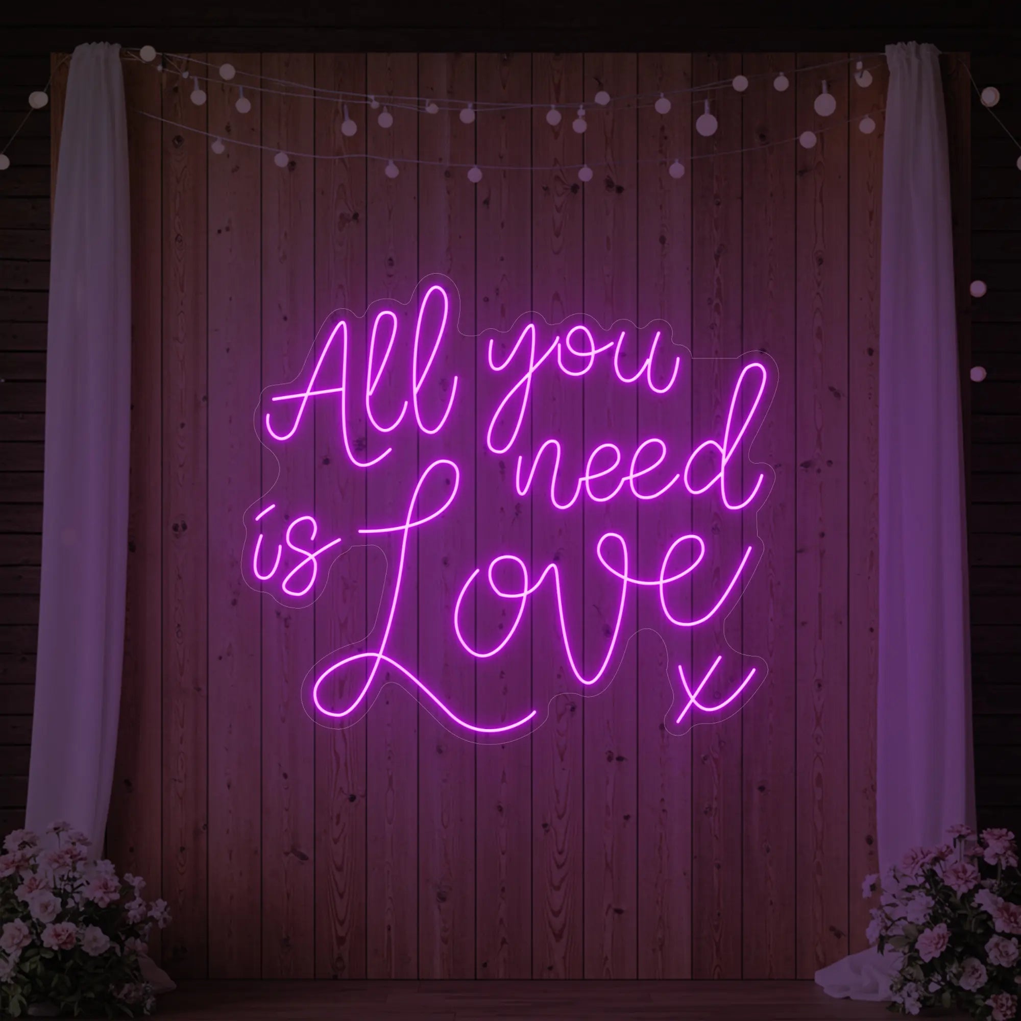 Photo of the 'All You Need Is Love V1' neon sign glowing in deep pink against a styled interior wall.