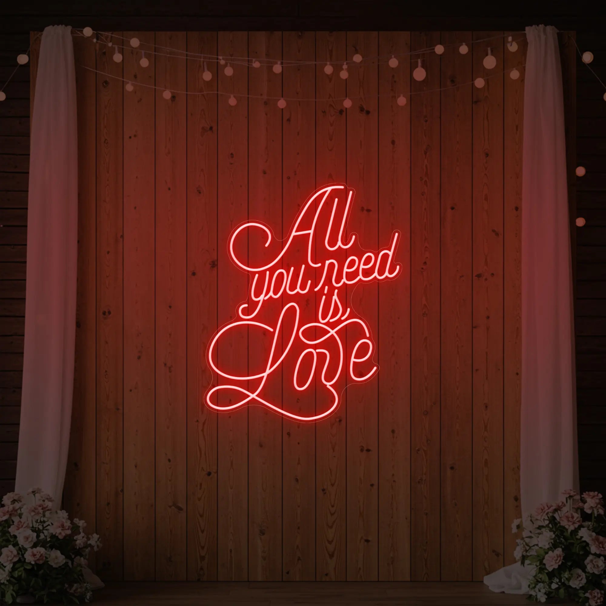 Photo of the 'All You Need Is Love V2' neon sign glowing in red against a styled interior wall.