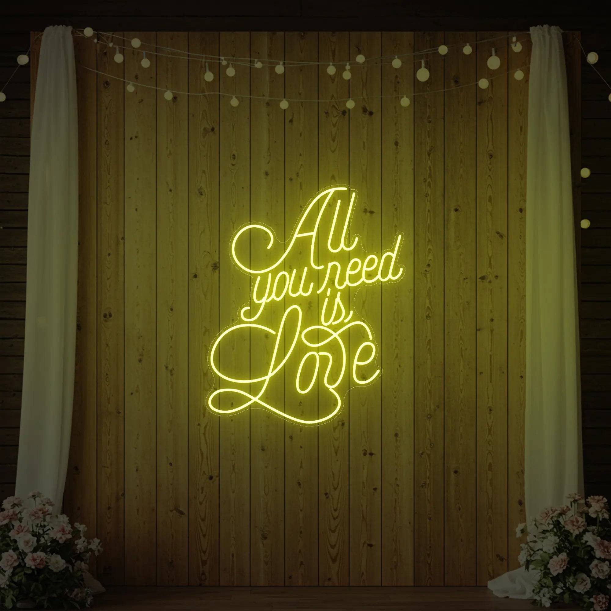 Photo of the 'All You Need Is Love V2' neon sign glowing in lemon yellow against a styled interior wall.