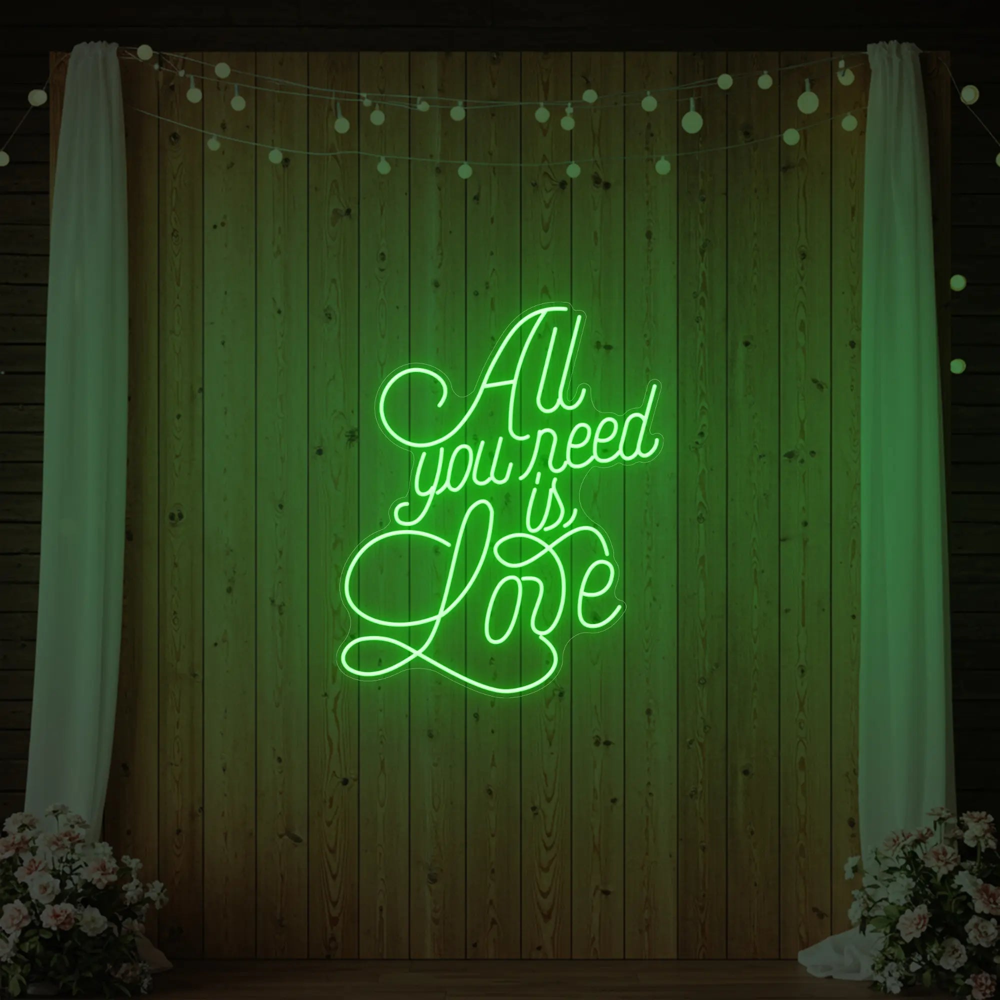 Photo of the 'All You Need Is Love V2' neon sign glowing in green against a styled interior wall.