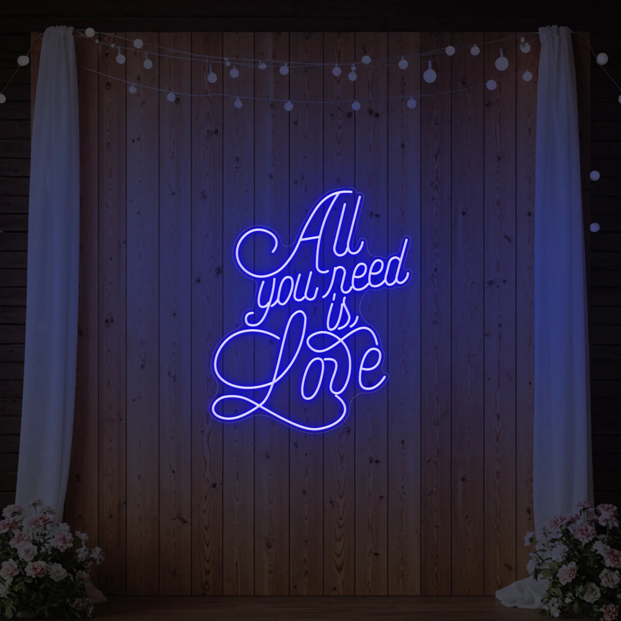 Photo of the 'All You Need Is Love V2' neon sign glowing in deep blue against a styled interior wall.
