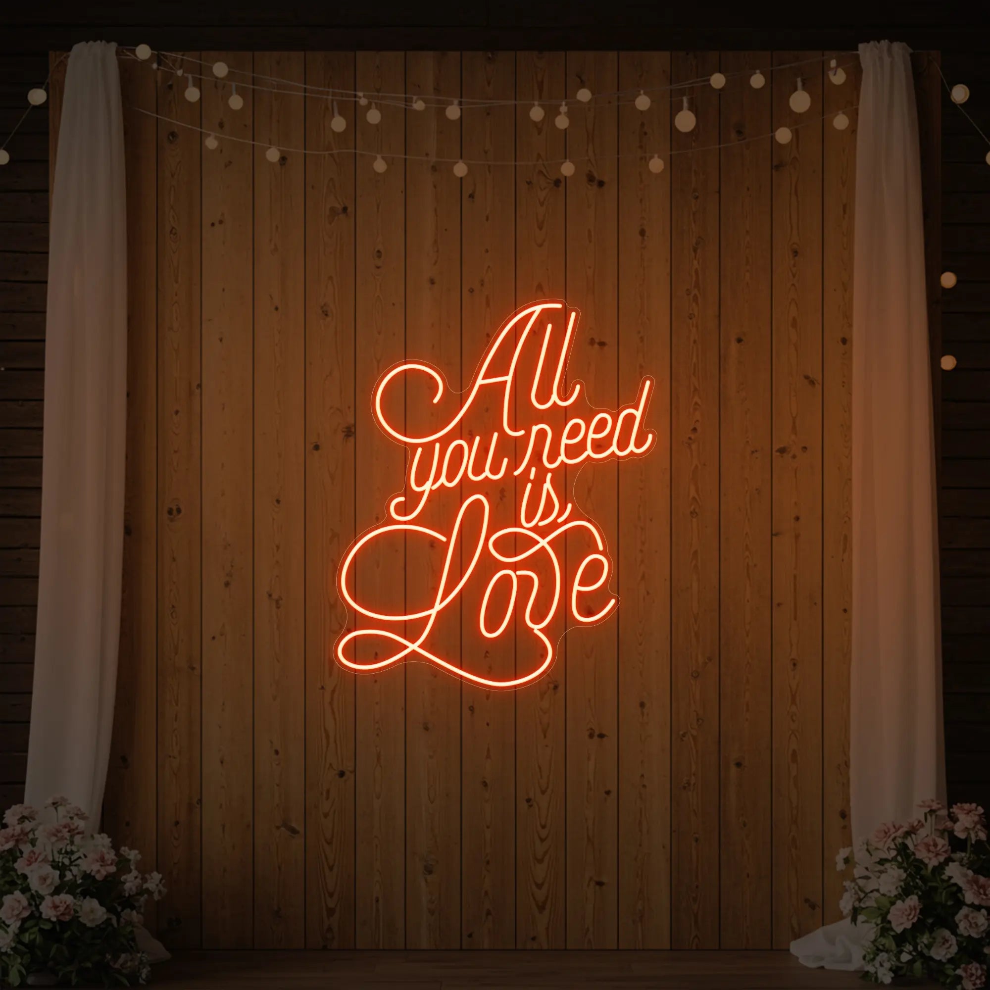 Photo of the 'All You Need Is Love V2' neon sign glowing in golden yellow against a styled interior wall.