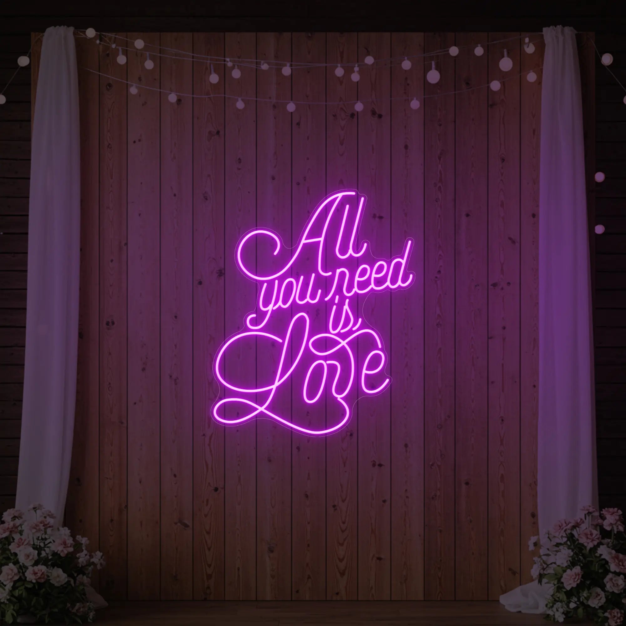 Photo of the 'All You Need Is Love V2' neon sign glowing in deep pink against a styled interior wall.
