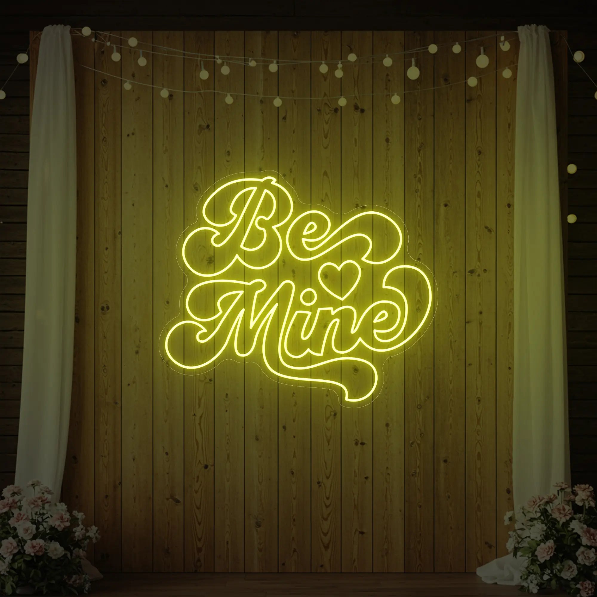 Photo of the 'Be Mine' neon sign glowing in lemon yellow against a styled interior wall.