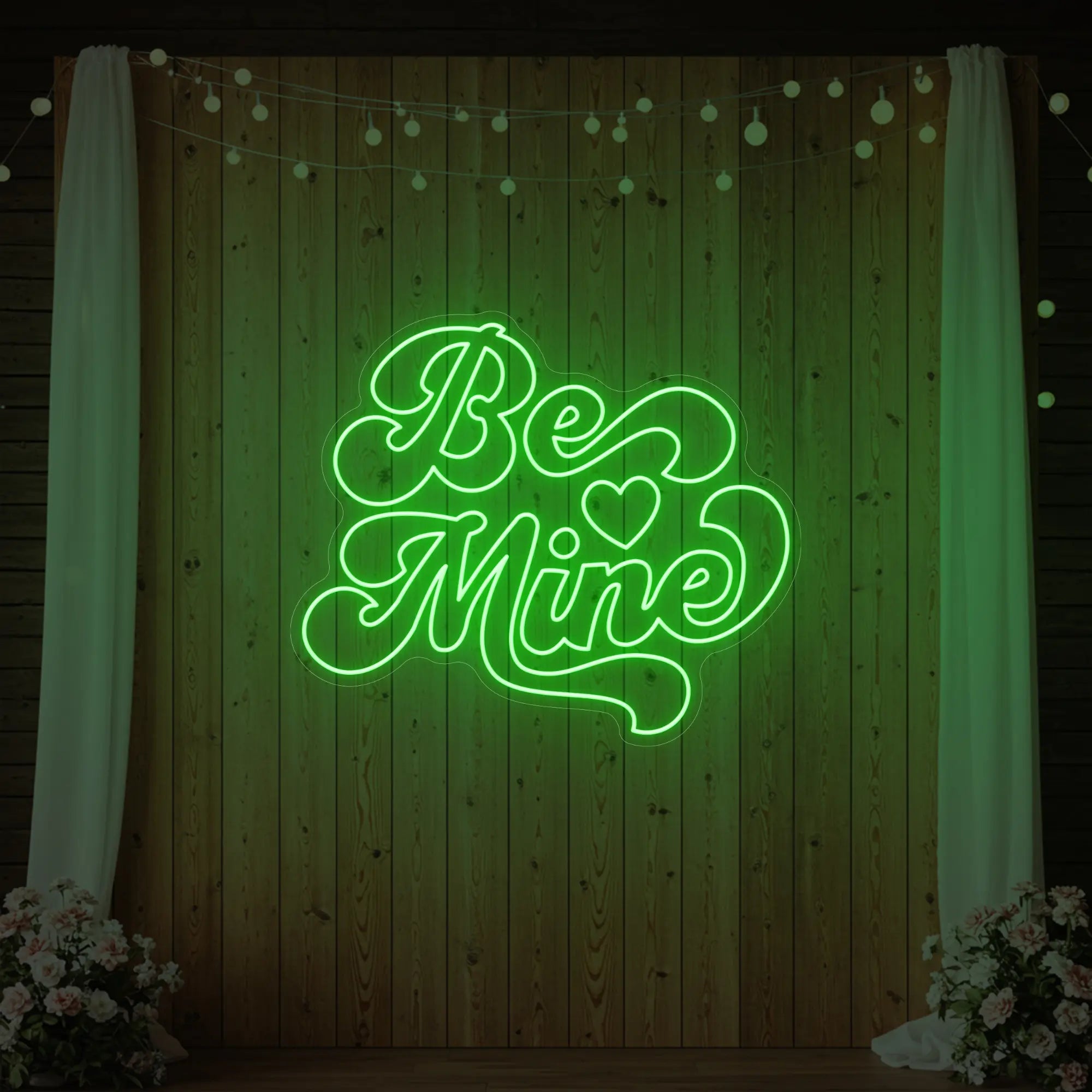 Photo of the 'Be Mine' neon sign glowing in green against a styled interior wall.