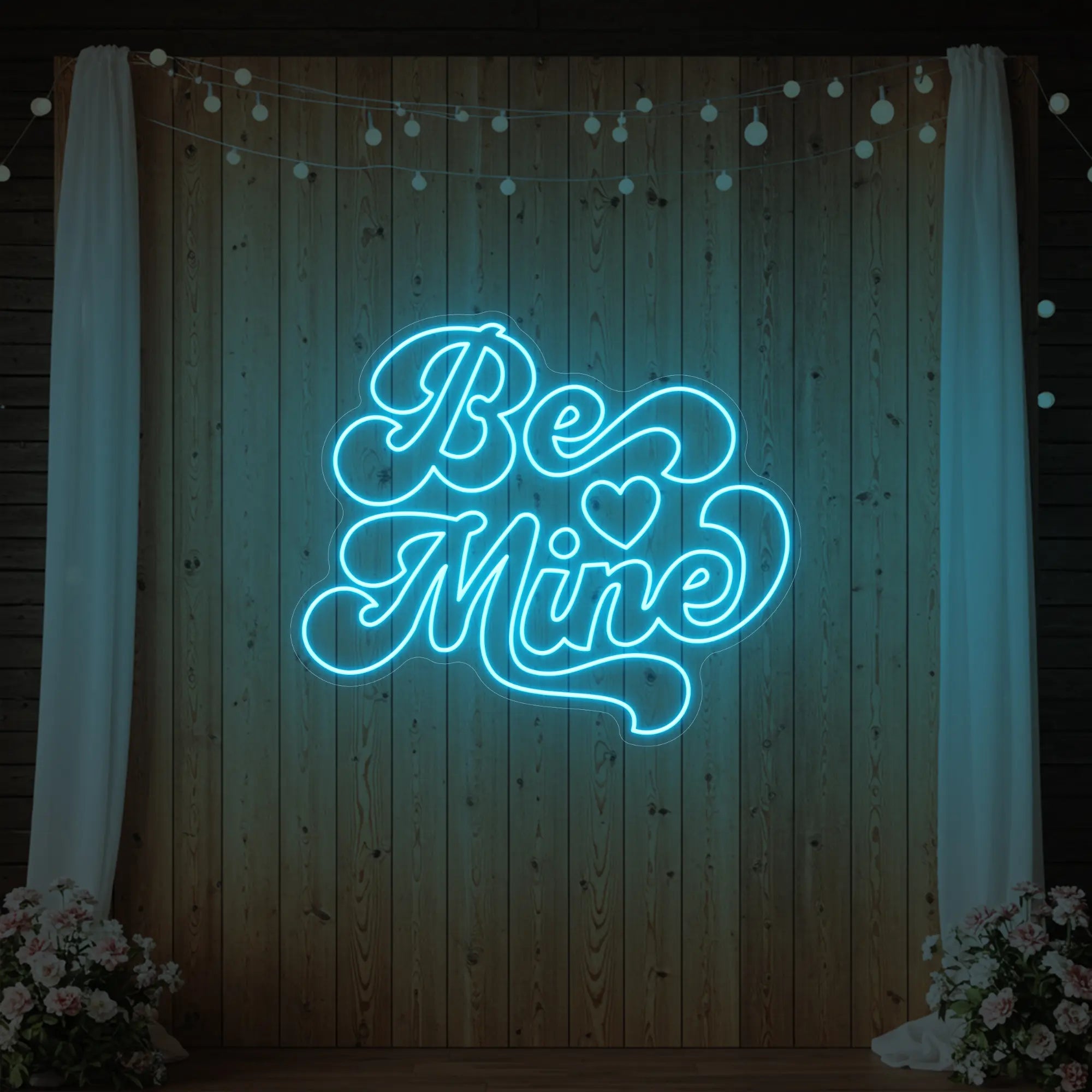 Photo of the 'Be Mine' neon sign glowing in ice blue against a styled interior wall.