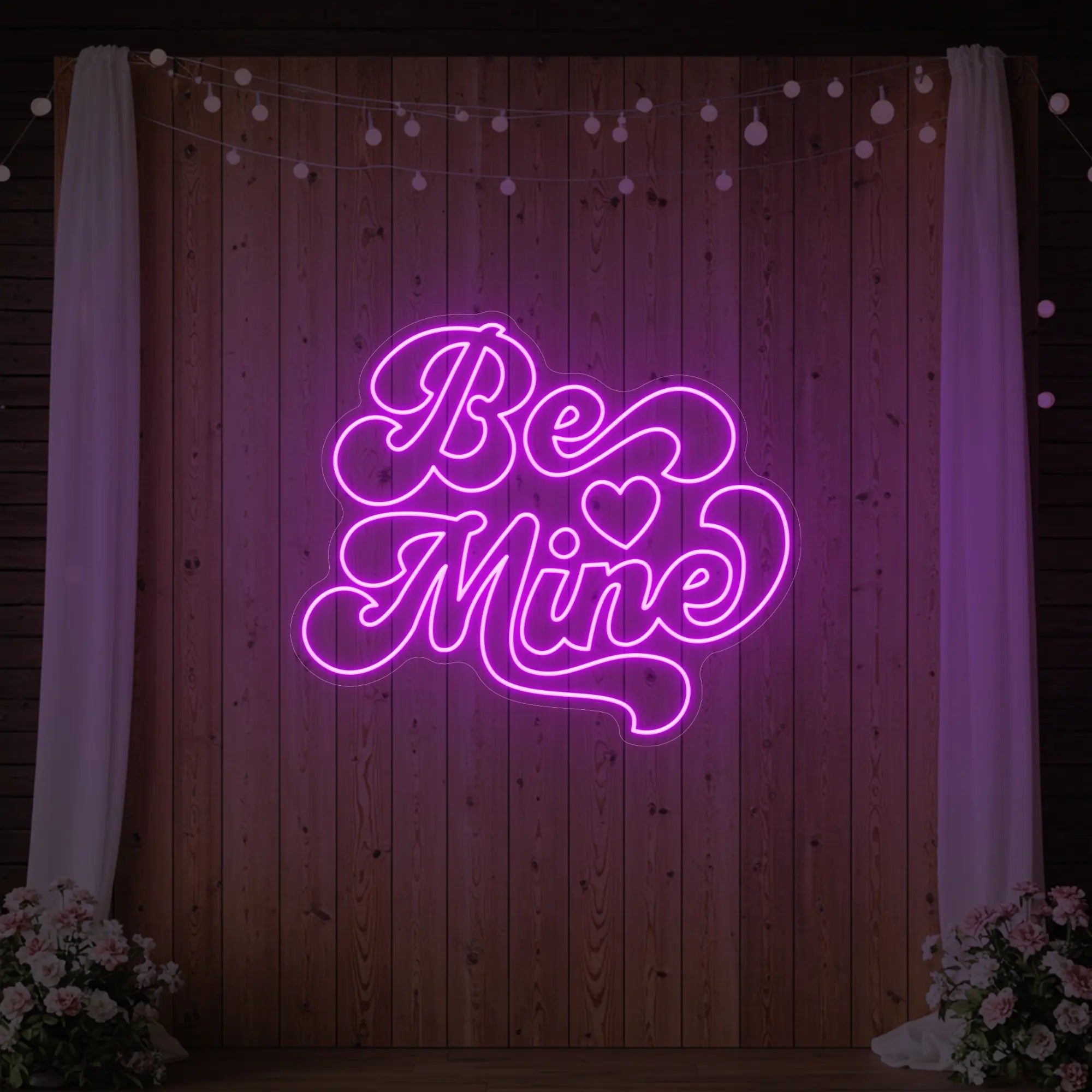 Photo of the 'Be Mine' neon sign glowing in deep pink against a styled interior wall.