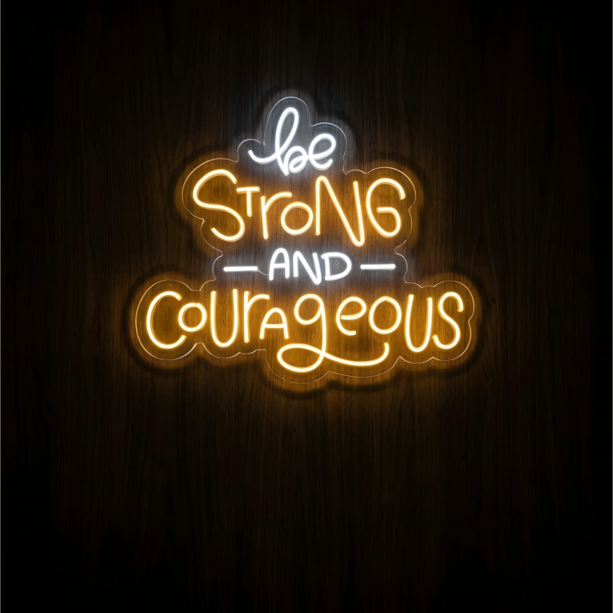 Be Strong and Courageous LED Neon Sign with warm yellow “Strong” and “Courageous” lettering and white “be” and “AND” on clear acrylic against a dark wood background, suited to bedrooms and home offices.