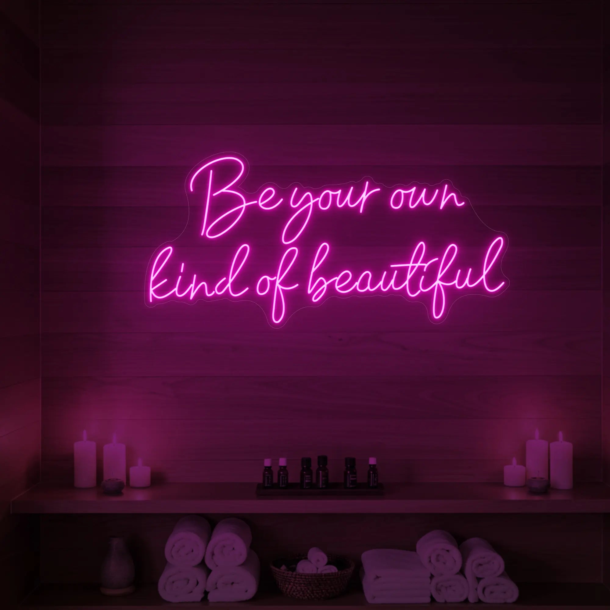 Photo of the 'Be Your Own Kind of Beautiful' neon sign glowing in light pink against a styled interior wall.