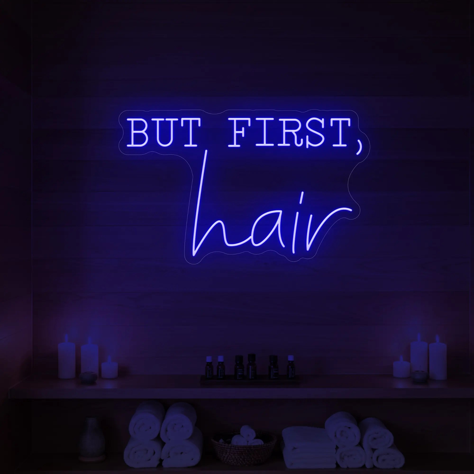 Photo of the 'BUT FIRST, hair' neon sign glowing in deep blue against a styled interior wall.