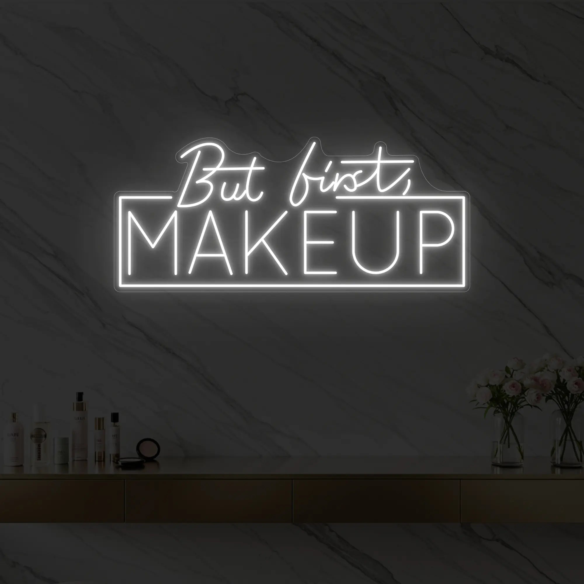 Photo of the 'But first, MAKEUP' neon sign glowing in cool white against a styled interior wall.