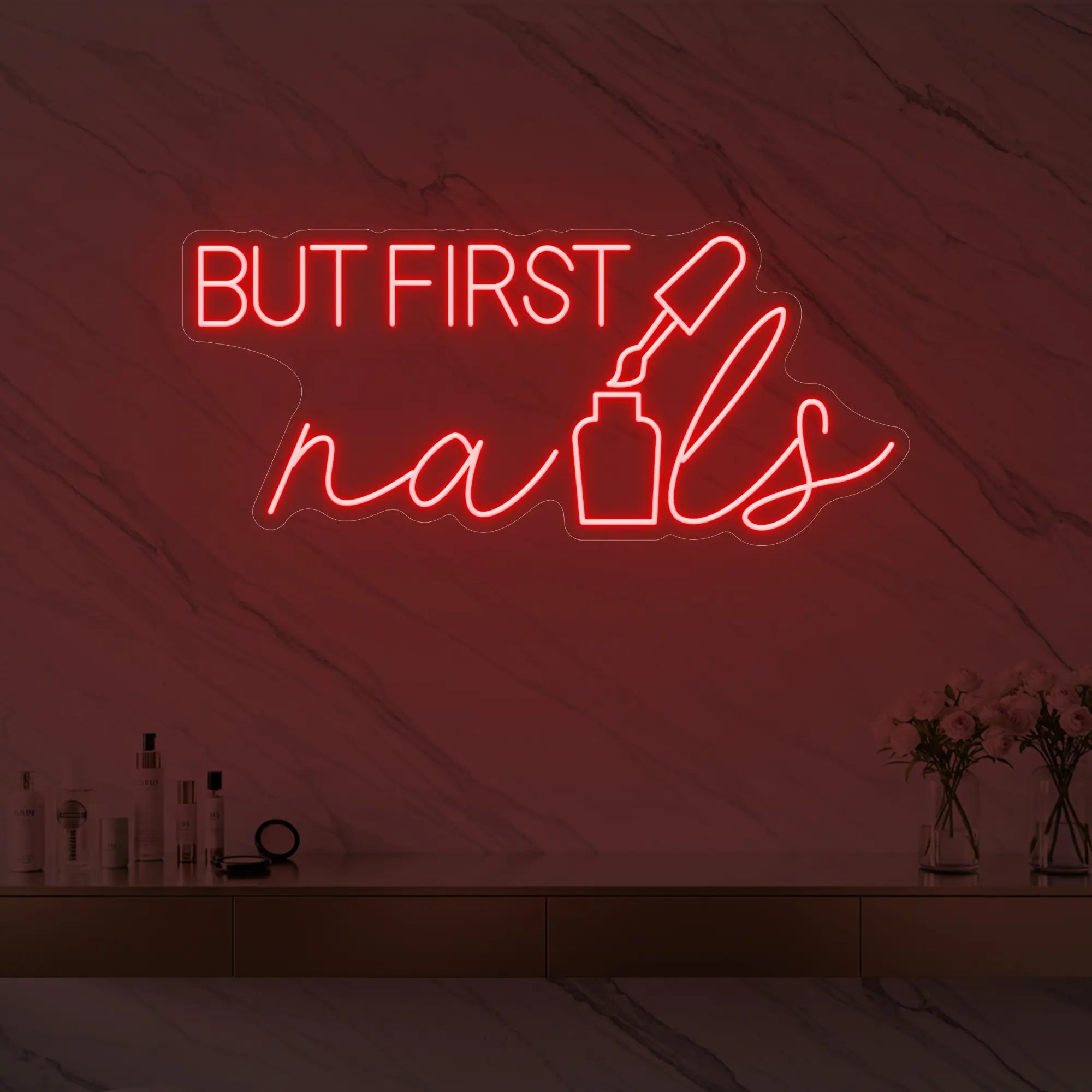 Photo of the 'BUT FIRST nails' neon sign with a nail polish bottle graphic glowing in red against a styled interior wall.