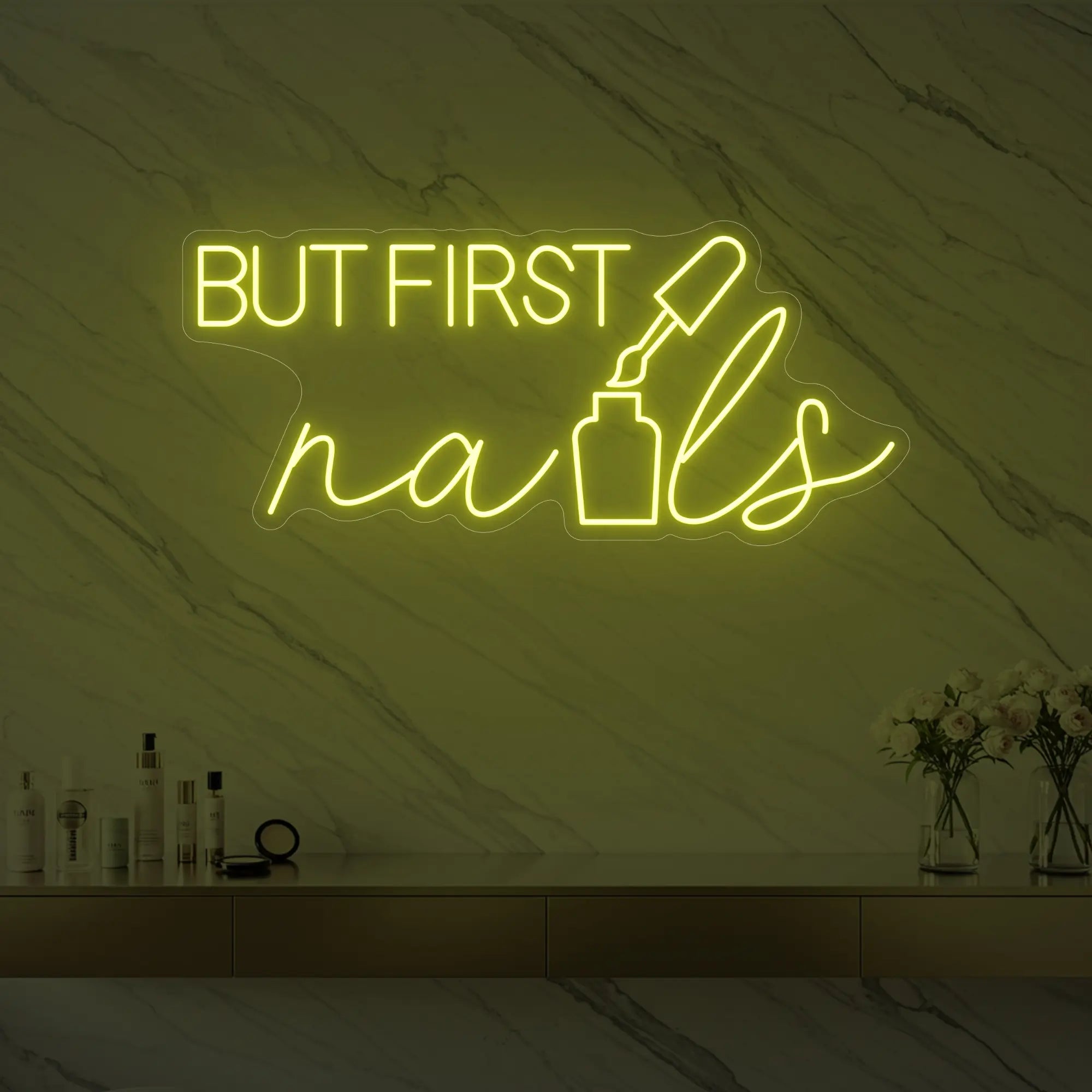 Photo of the 'BUT FIRST nails' neon sign with a nail polish bottle graphic glowing in lemon yellow against a styled interior wall.