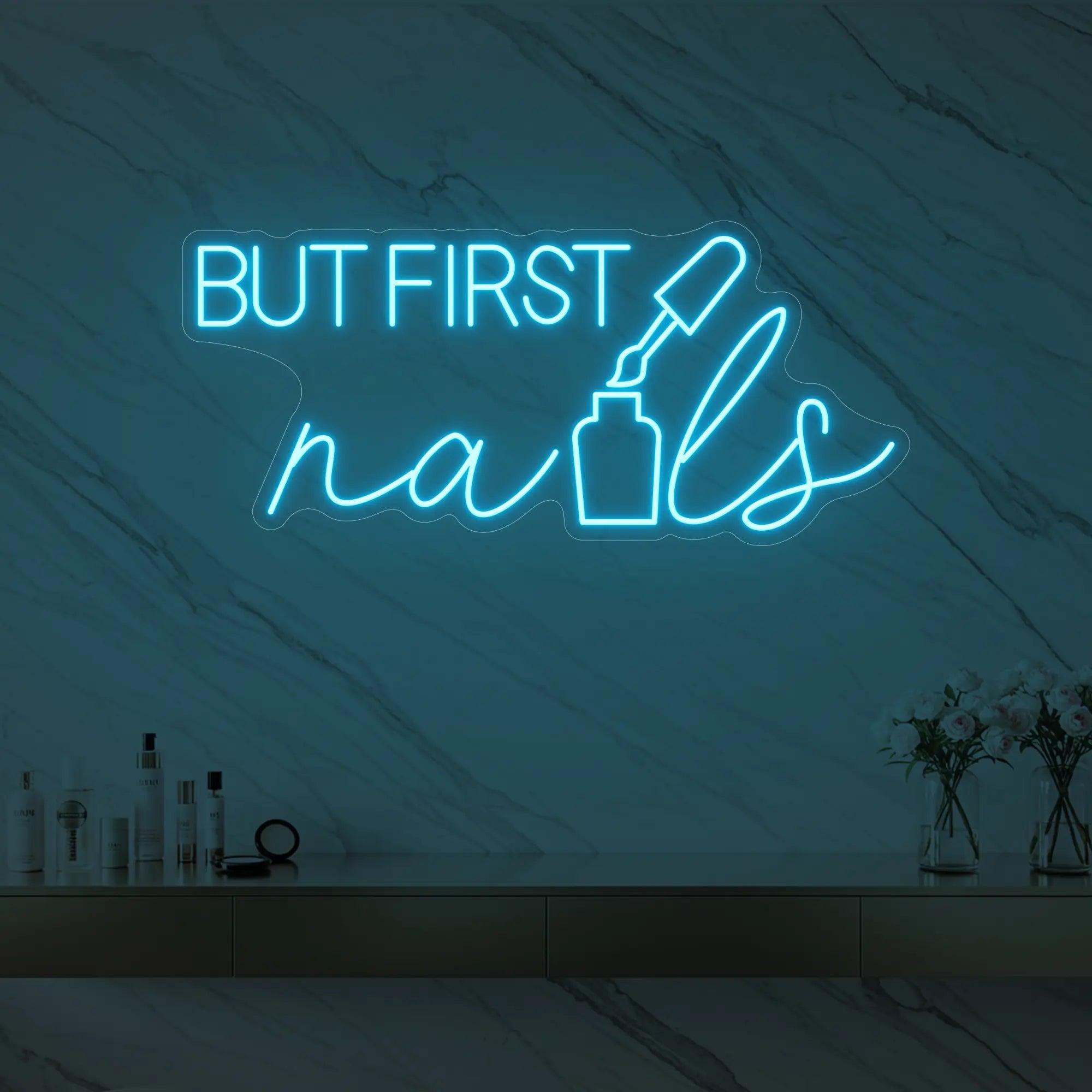 Photo of the 'BUT FIRST nails' neon sign with a nail polish bottle graphic glowing in ice blue against a styled interior wall.