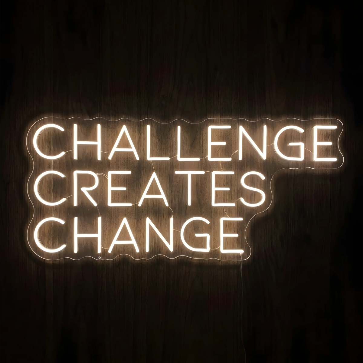 “CHALLENGE CREATES CHANGE” LED Neon Sign glowing in warm white uppercase letters across three lines on clear acrylic against a dark wood background, suited to home offices and fitness spaces.