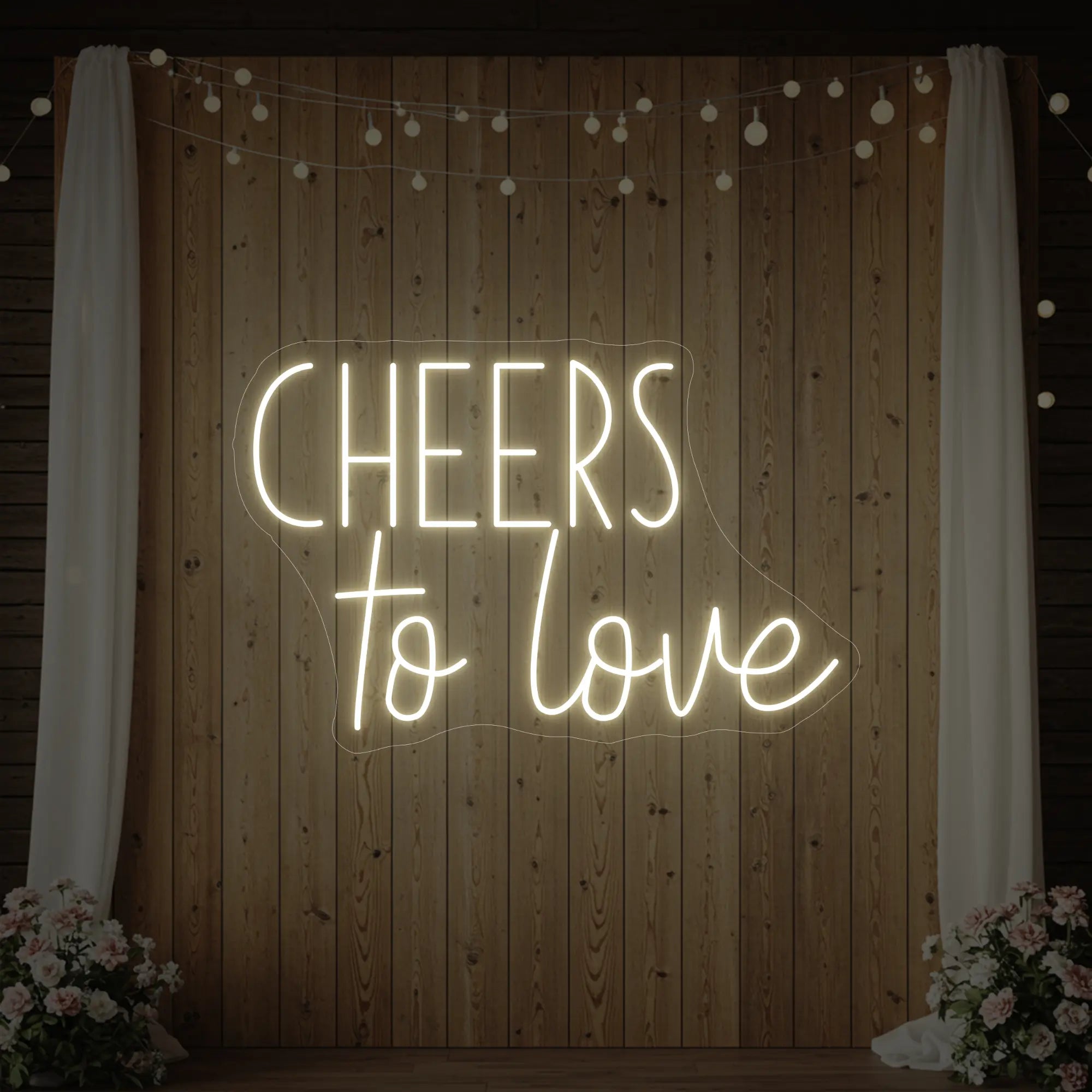 Photo of the 'Cheers To Love' neon sign glowing in warm white against a styled interior wall.