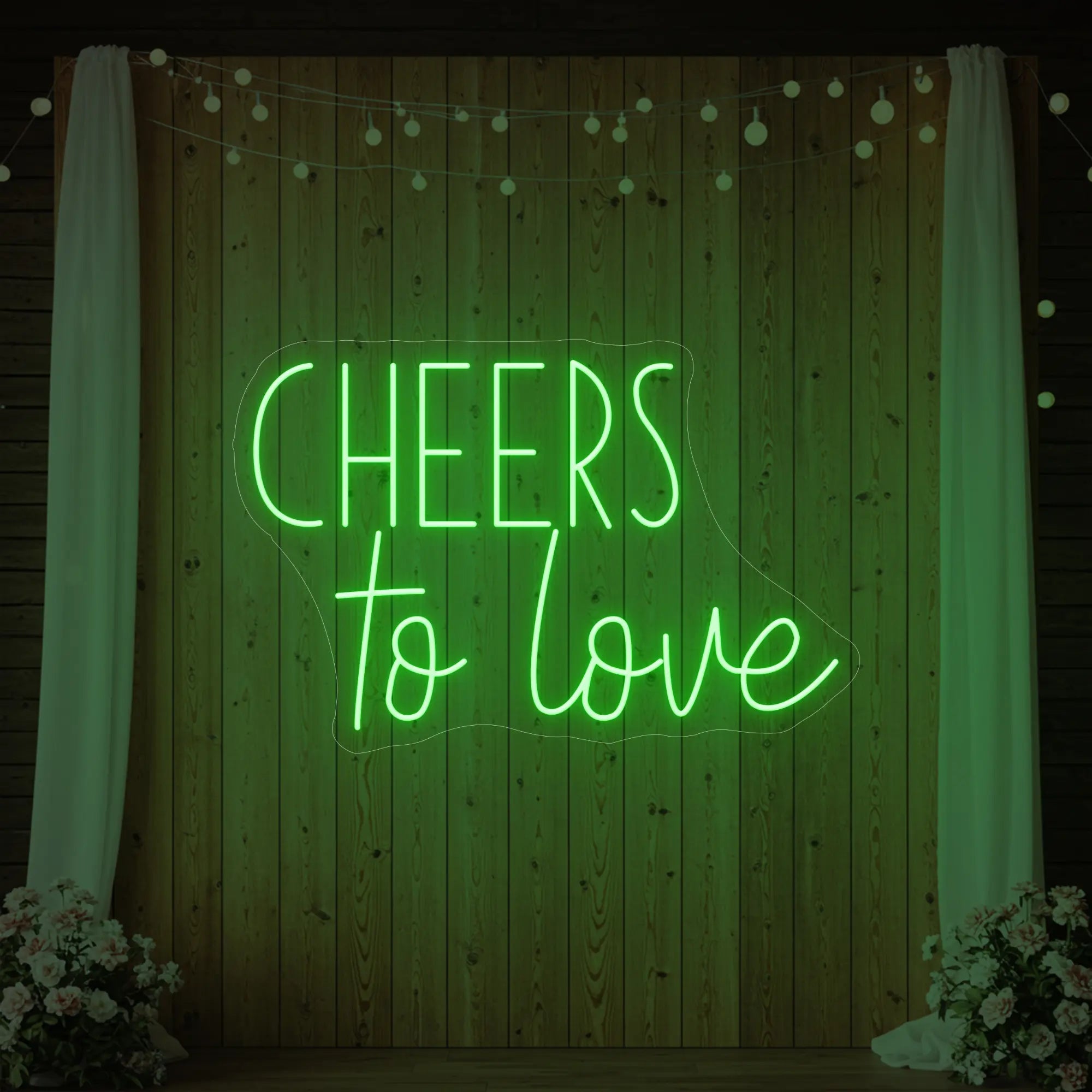Photo of the 'Cheers To Love' neon sign glowing in green against a styled interior wall.