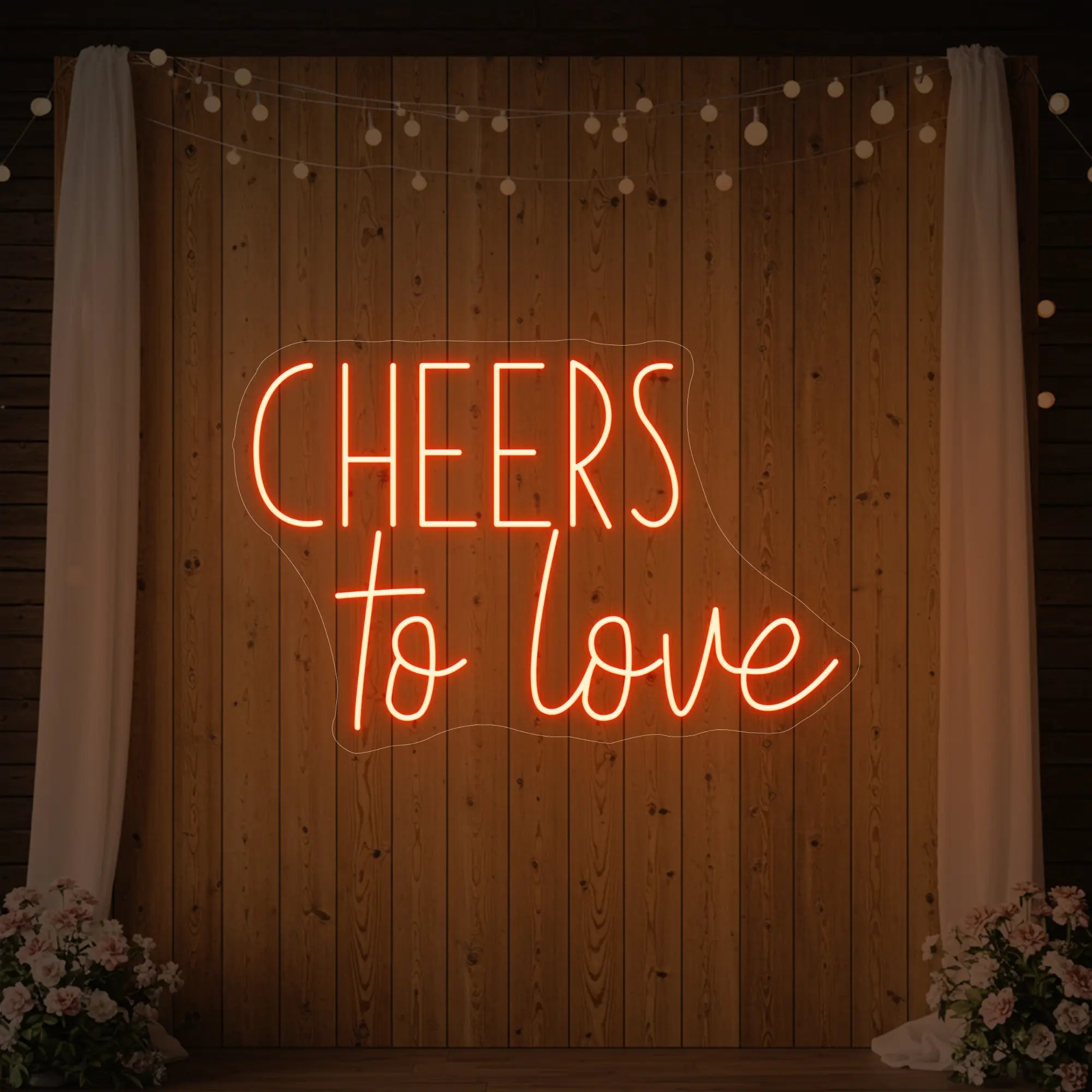 Photo of the 'Cheers To Love' neon sign glowing in golden yellow against a styled interior wall.