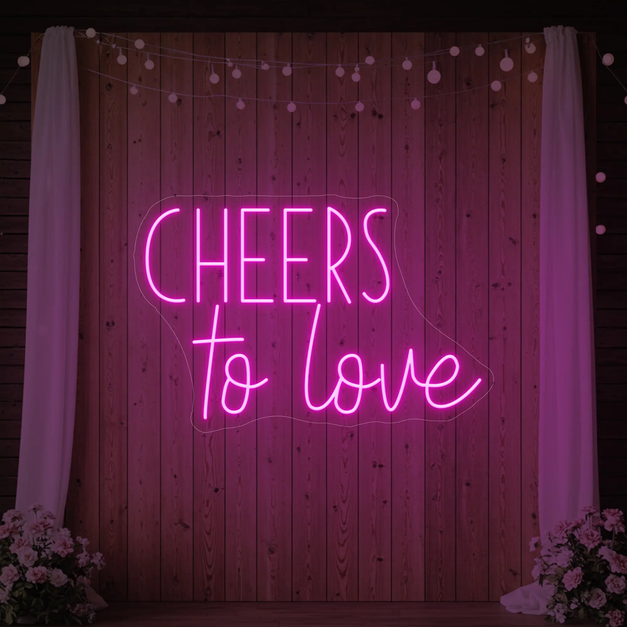 Photo of the 'Cheers To Love' neon sign glowing in light pink against a styled interior wall.