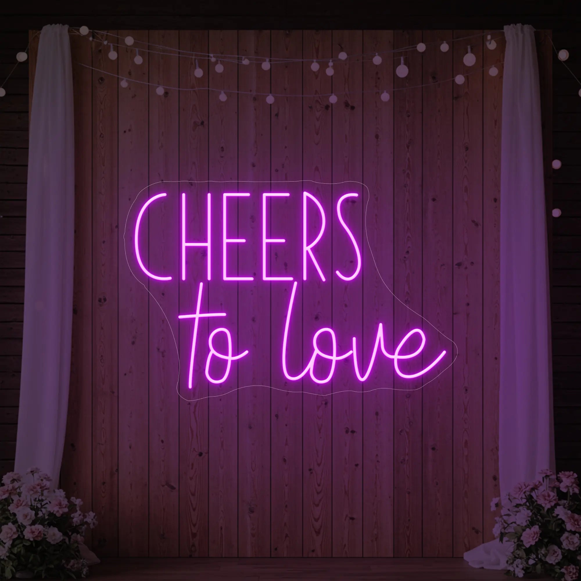 Photo of the 'Cheers To Love' neon sign glowing in deep pink against a styled interior wall.