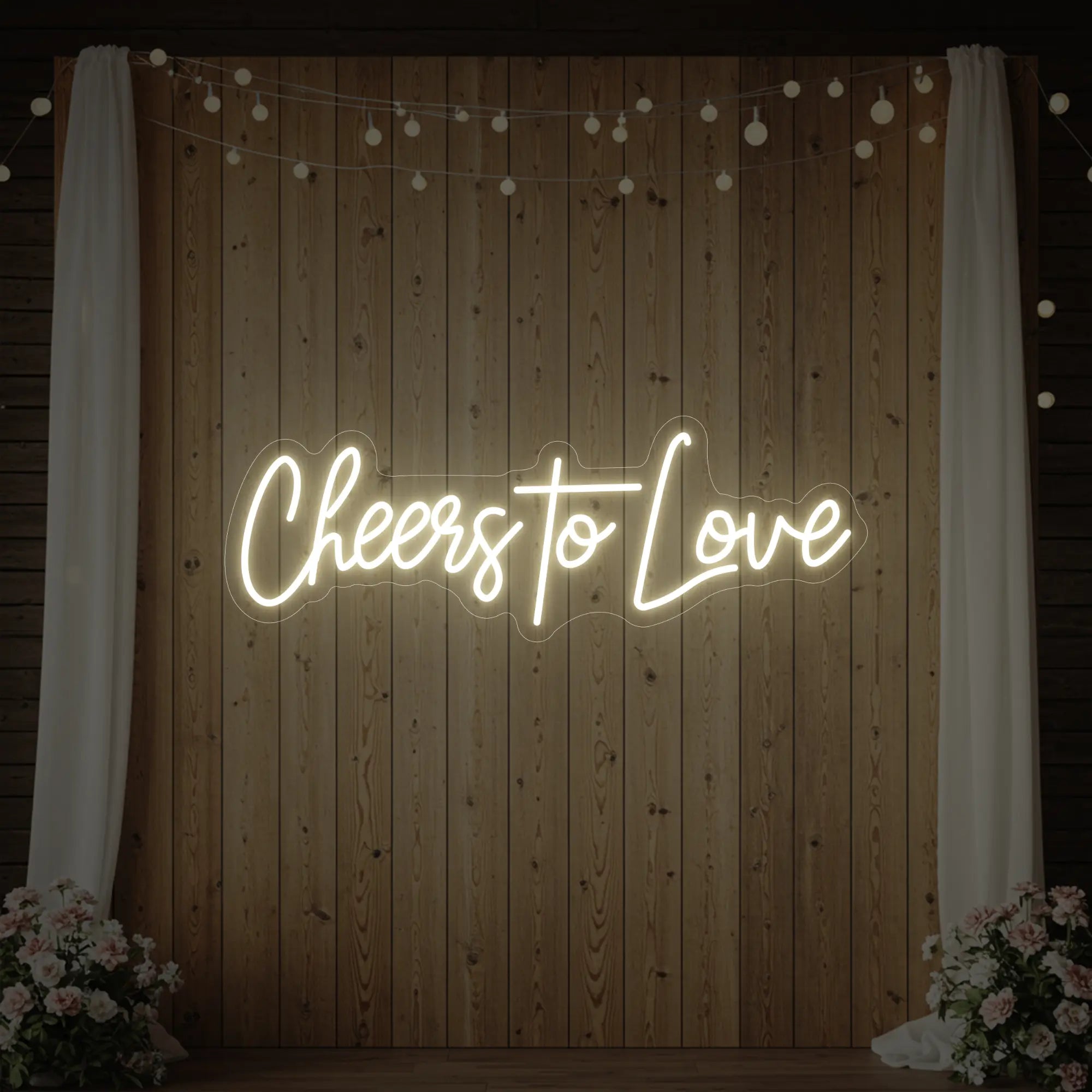 Photo of the 'Cheers To Love' neon sign glowing in warm white against a styled interior wall.