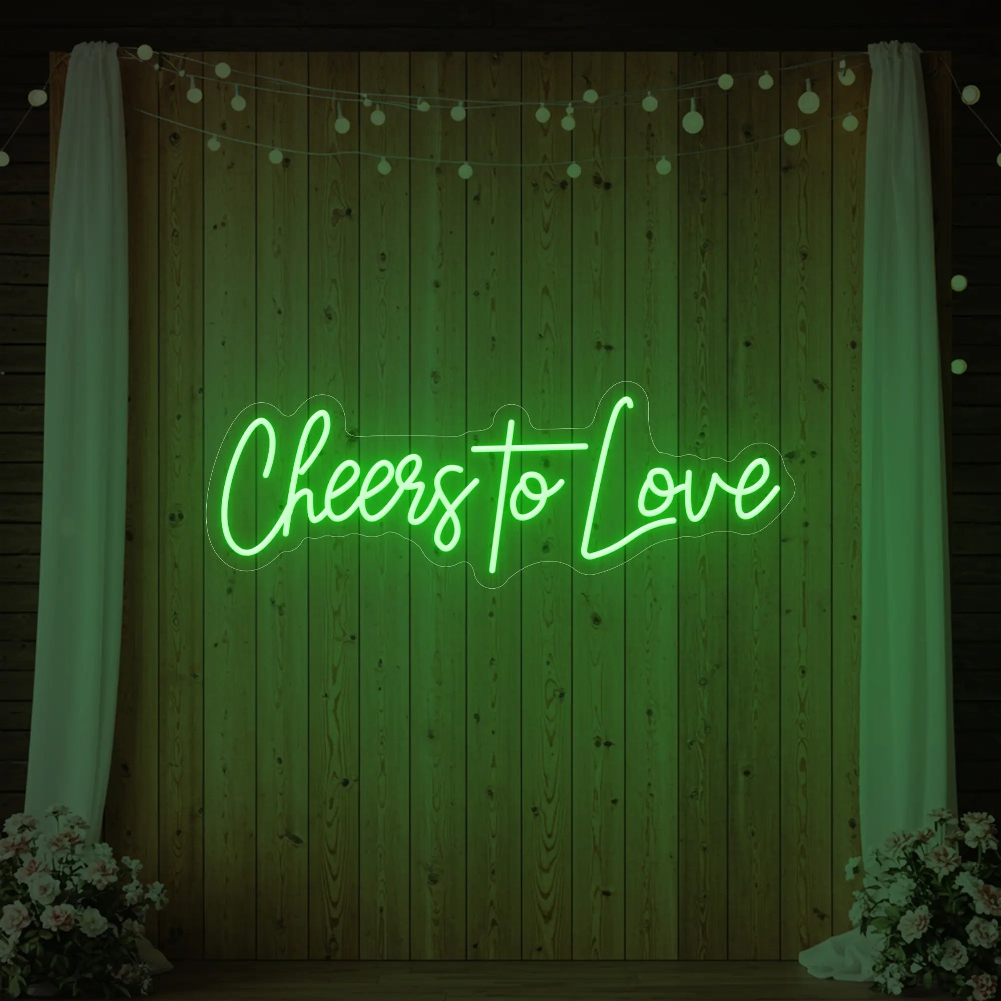Photo of the 'Cheers To Love' neon sign glowing in green against a styled interior wall.