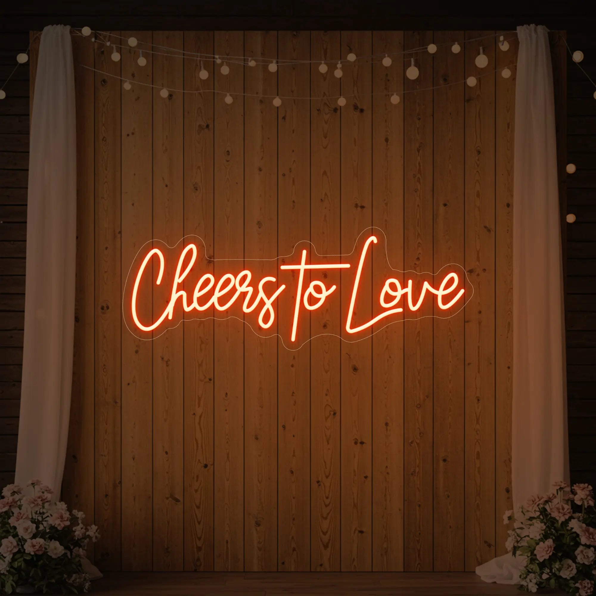 Photo of the 'Cheers To Love' neon sign glowing in golden yellow against a styled interior wall.