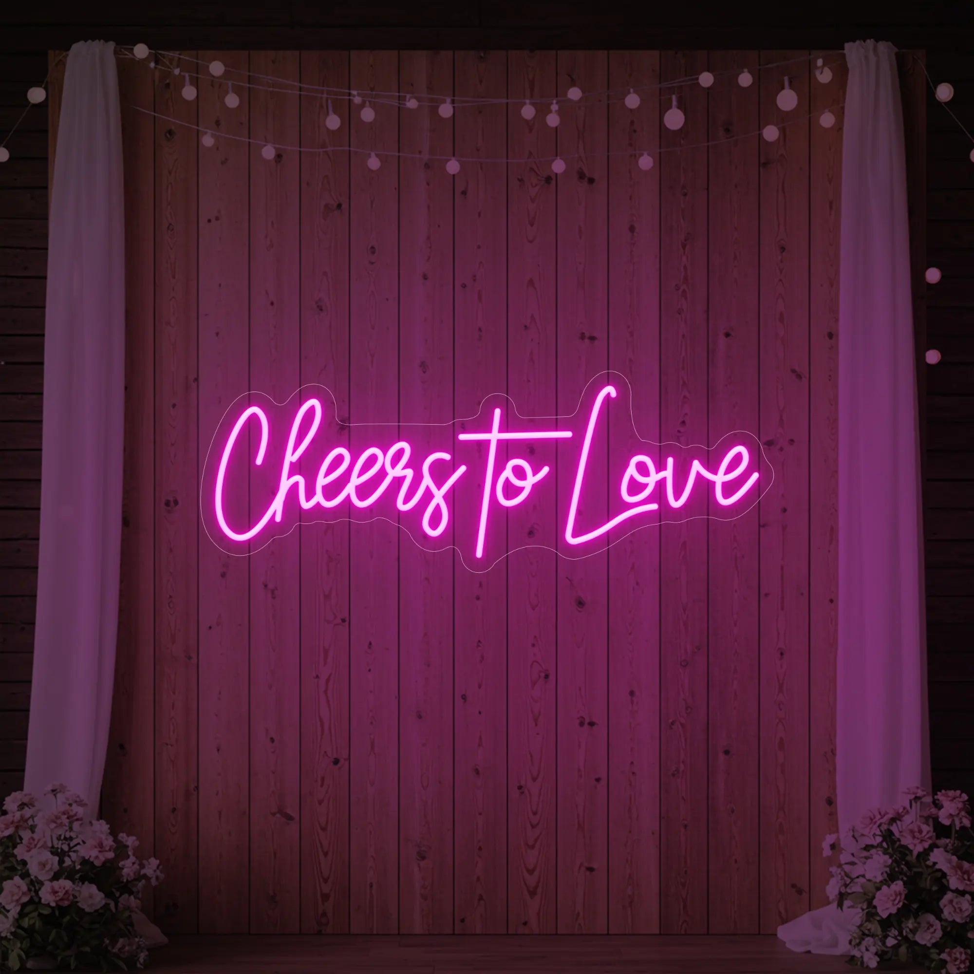 Photo of the 'Cheers To Love' neon sign glowing in light pink against a styled interior wall.