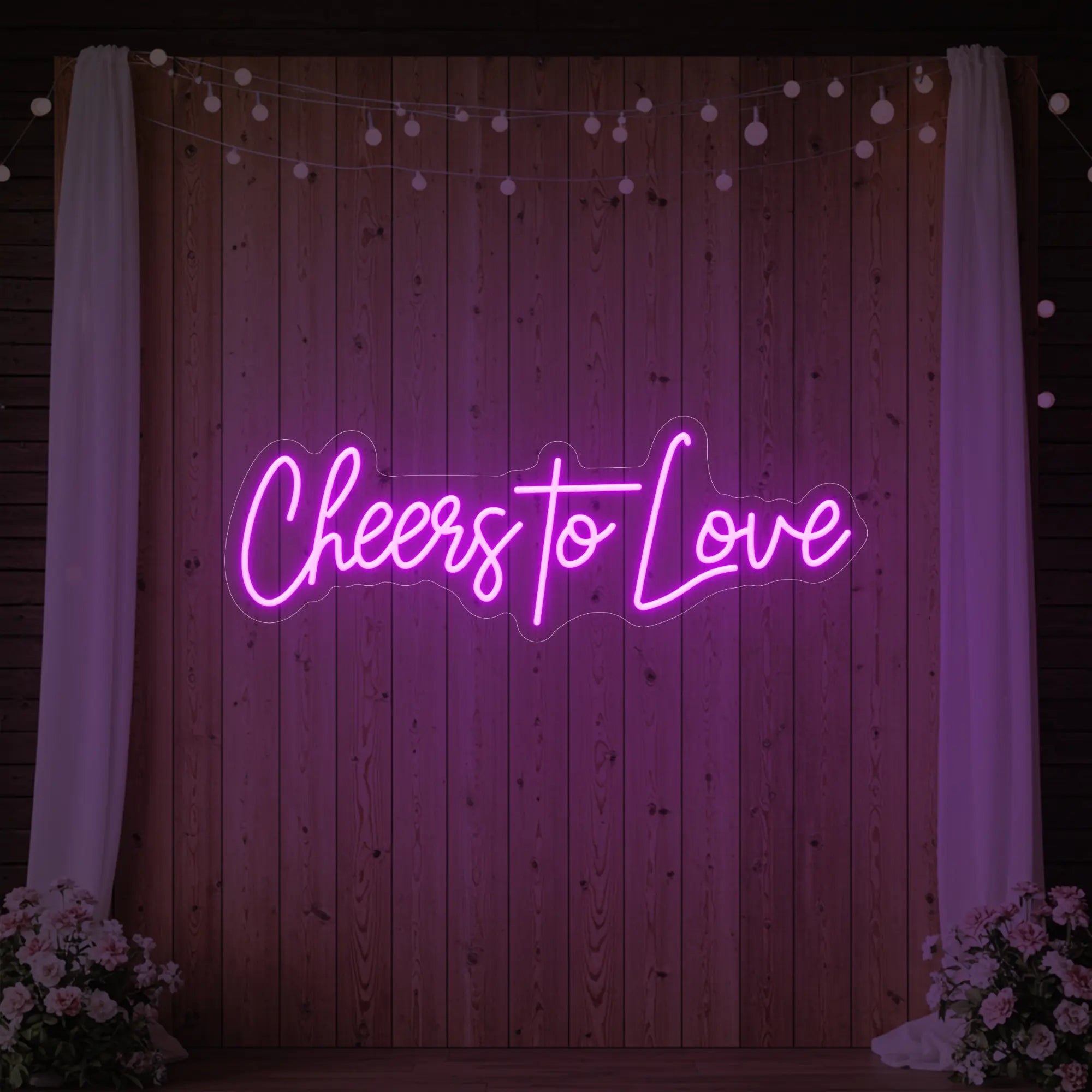 Photo of the 'Cheers To Love' neon sign glowing in deep pink against a styled interior wall.