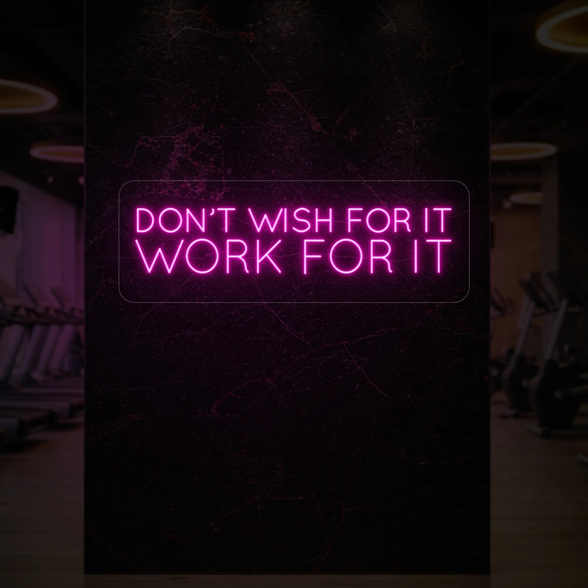 'Don’t Wish For It, Work For It' neon sign glowing in light pink against a styled interior wall.