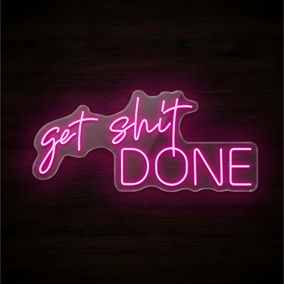 “Get Shit Done” LED Neon Sign glowing in bright pink, with script lettering above large uppercase text, mounted on clear acrylic against a dark wood background, ideal for home offices and creative workspaces.